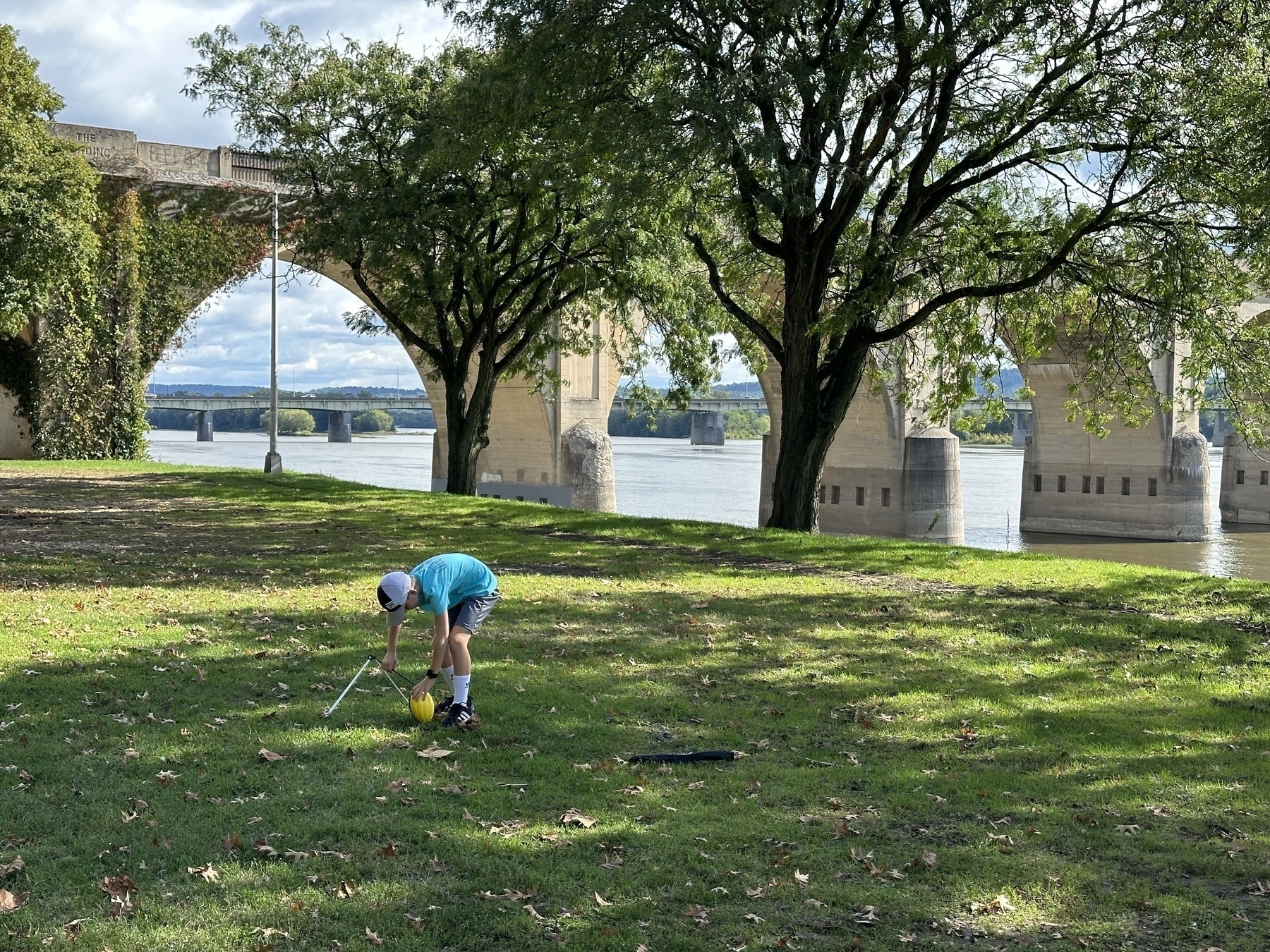 Mozzie setting up the football to kick at Riverfront Park in harrisburg pennsylvania. River and arch bridge in the background.