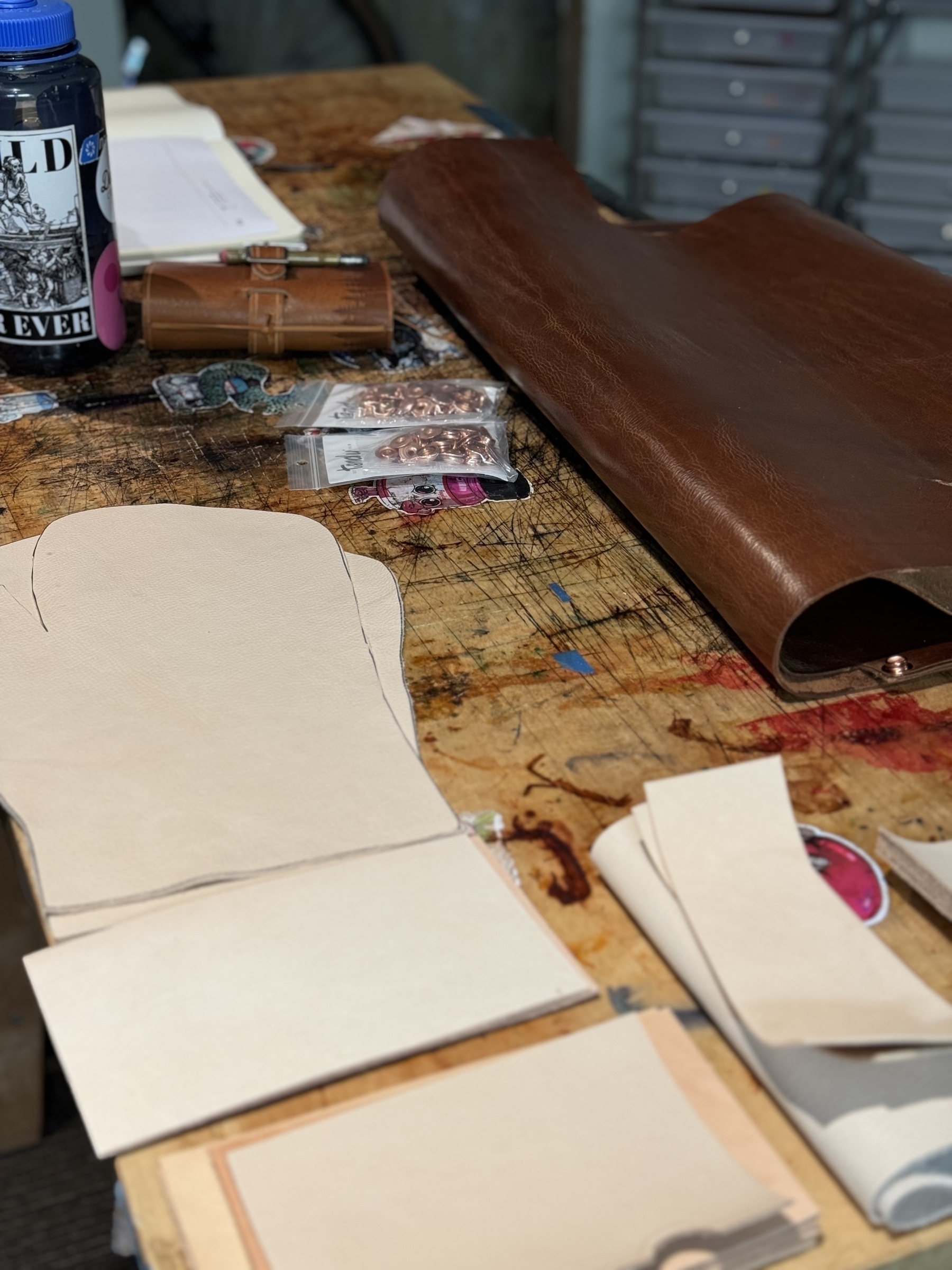 A workspace with leather and paper patterns, along with various crafting tools and materials, is displayed.