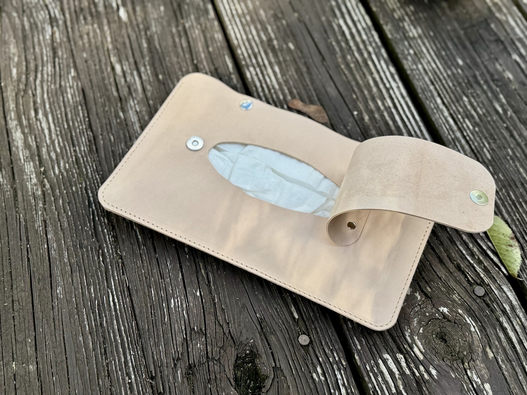 A light-colored leather or suede pouch is laid open on a weathered wooden surface.