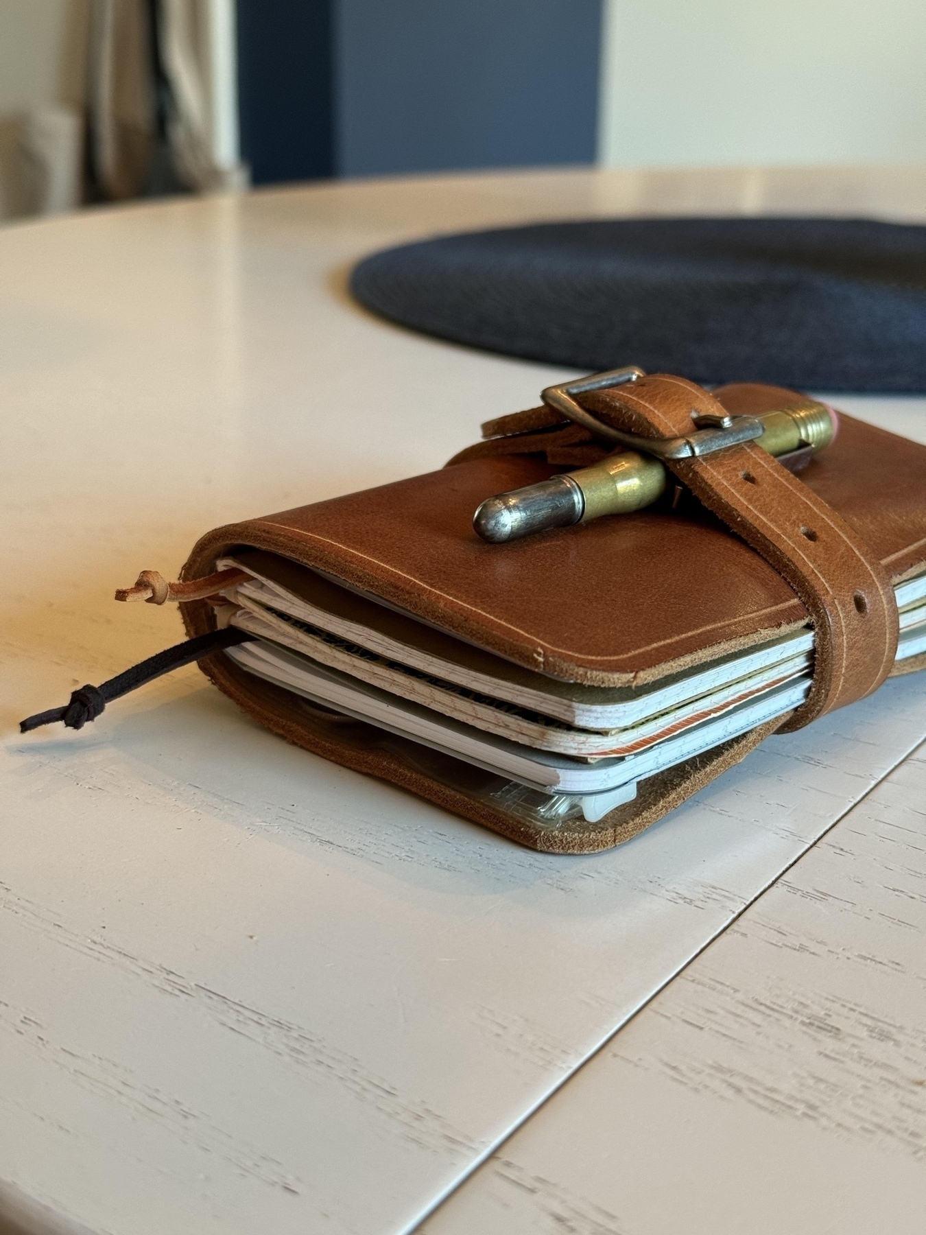 A leather-bound journal with a pen attached by a strap rests on a white table.