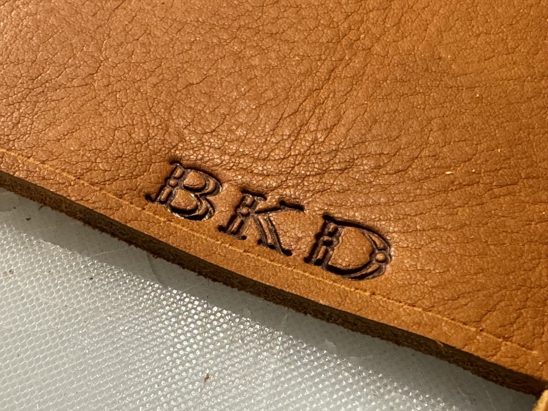 A piece of brown leather is embossed with the initials "BKD."