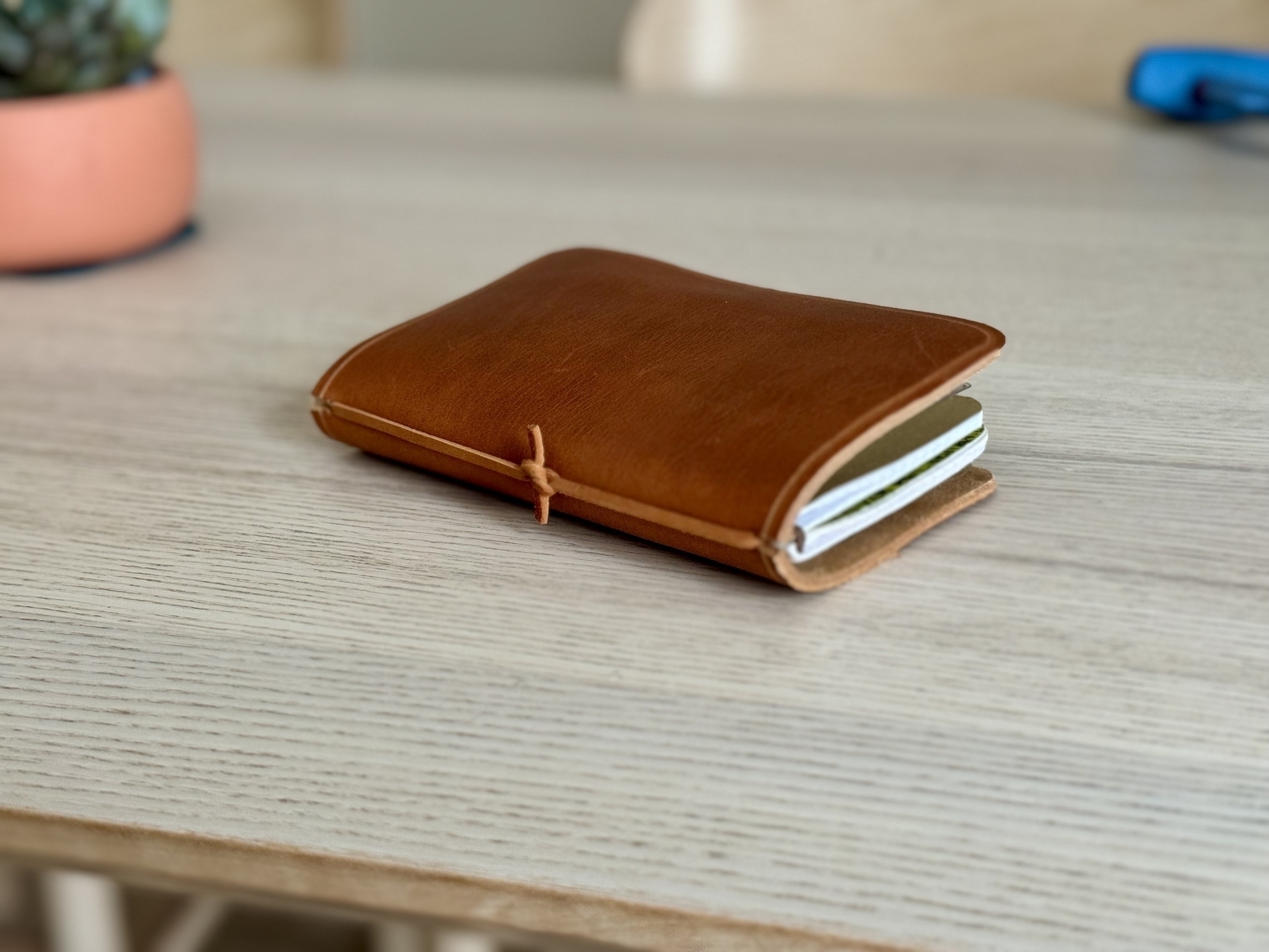 A brown leather notebook with some pages visible is resting on a light wooden table.