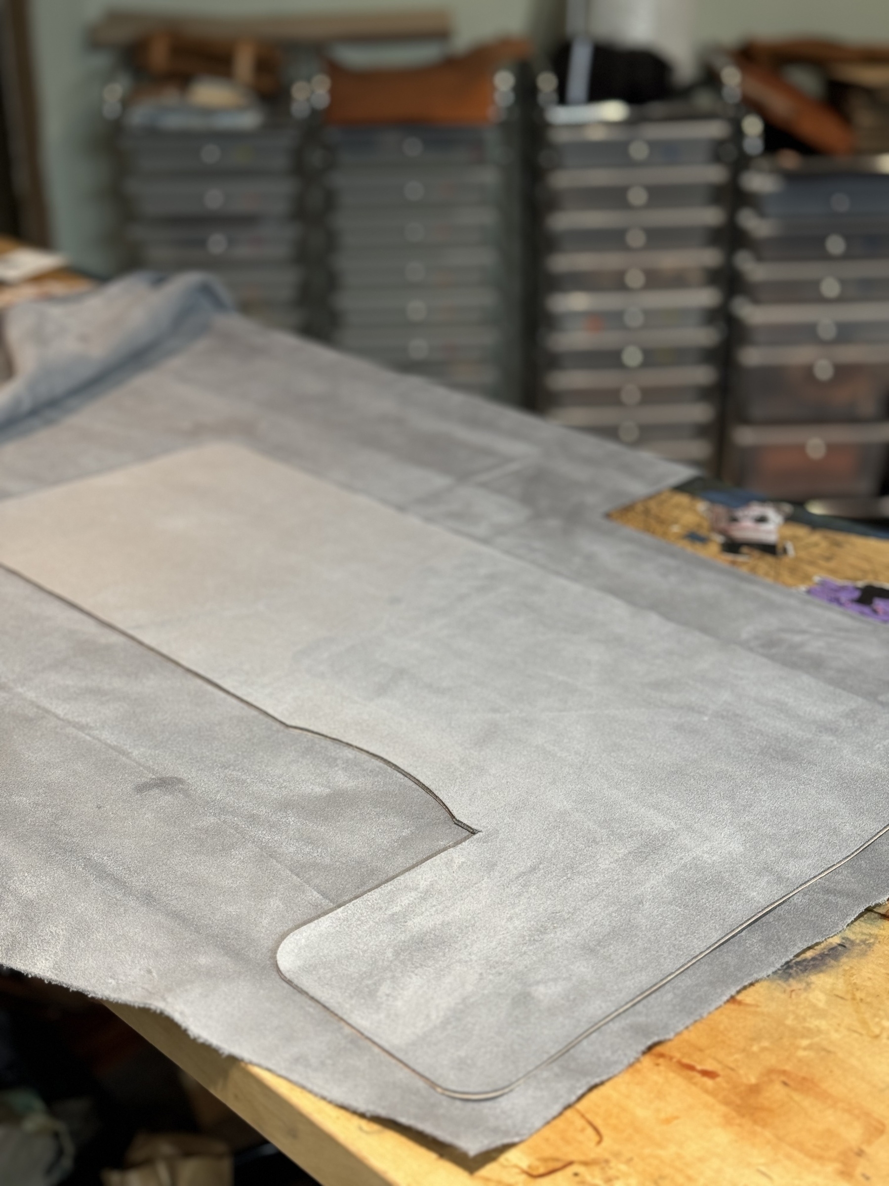 A piece of suede with pattern cutout lies on a workbench in front of stacked drawers.