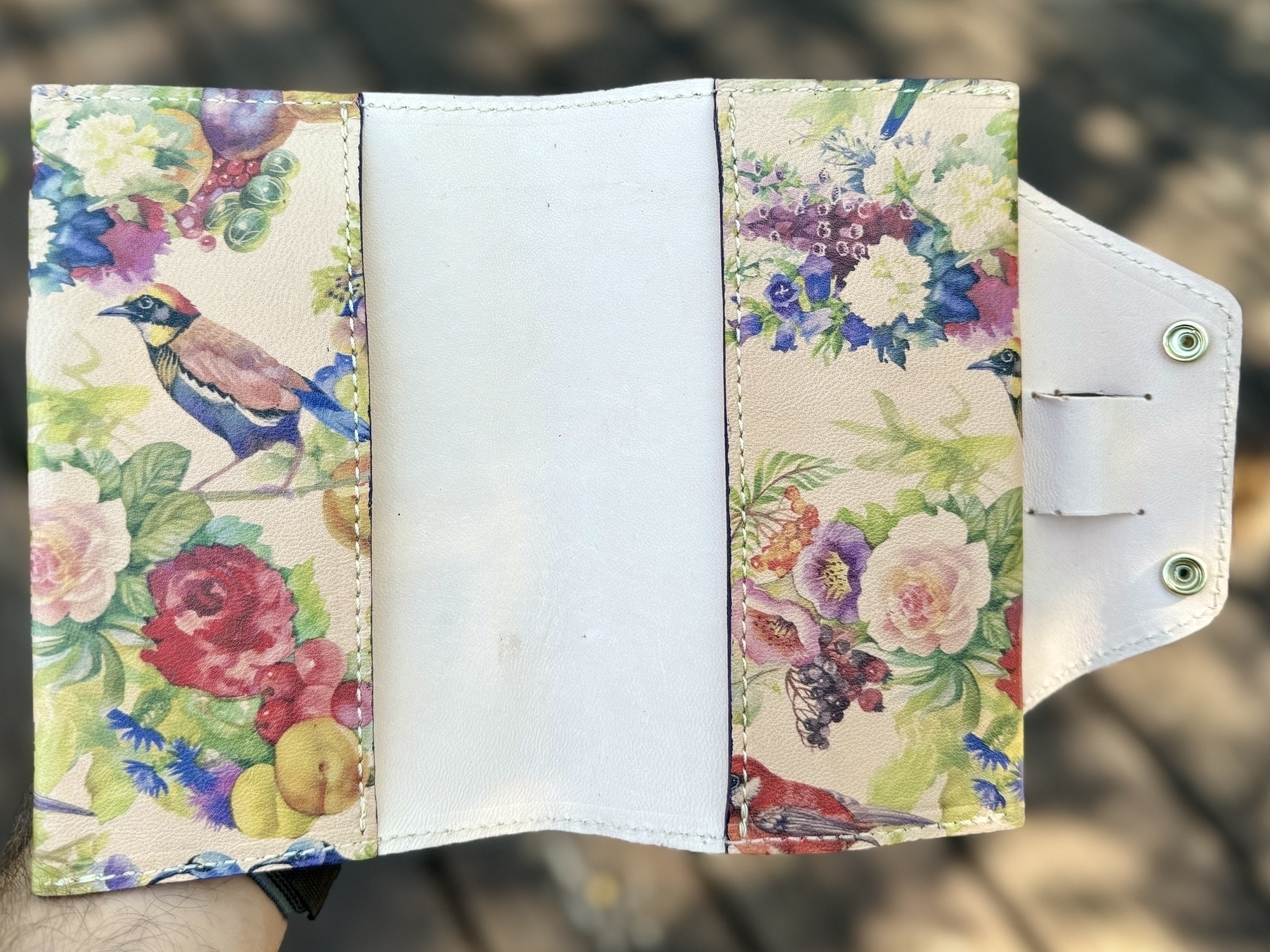 A floral and bird patterned wallet with two side flaps and a central pocket is open, displaying its interior.