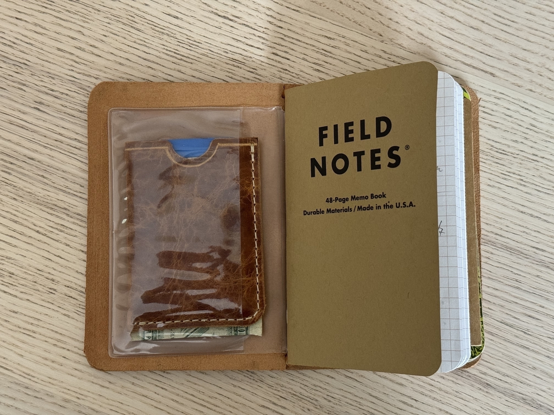 A memo book titled "Field Notes" and a brown leather cardholder are placed on a wooden surface.