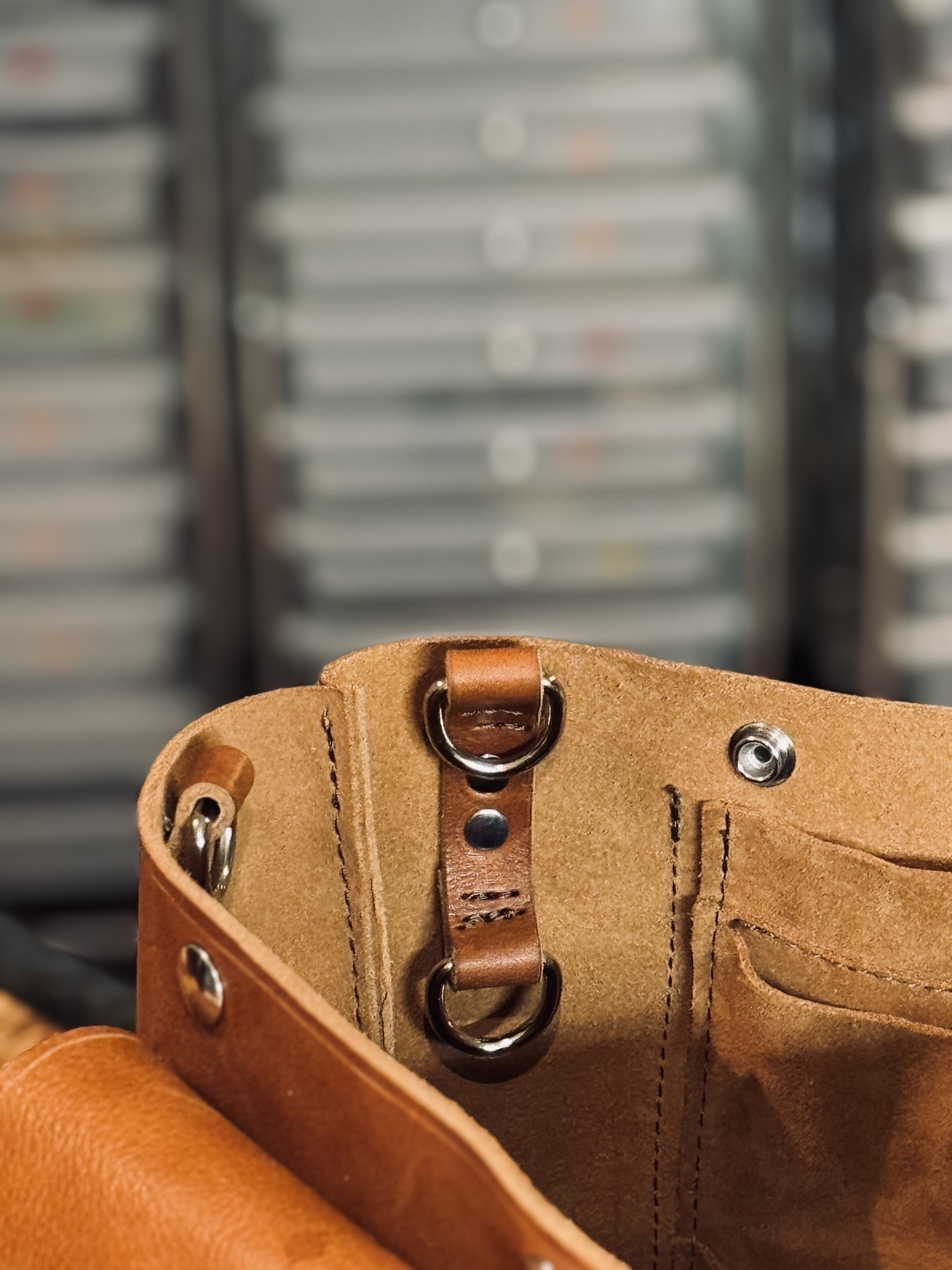 A close-up of the inside of a brown leather bag with metal rivets and rings on a blurred background of organized drawers.