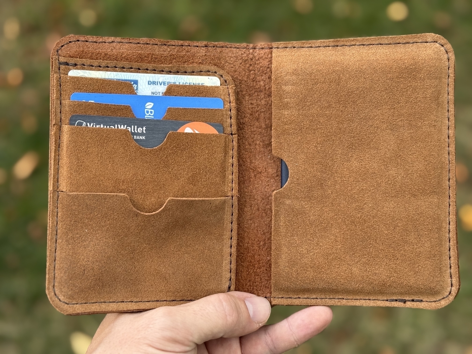 A hand holding an open brown leather passport case displaying multiple cards in its slots.