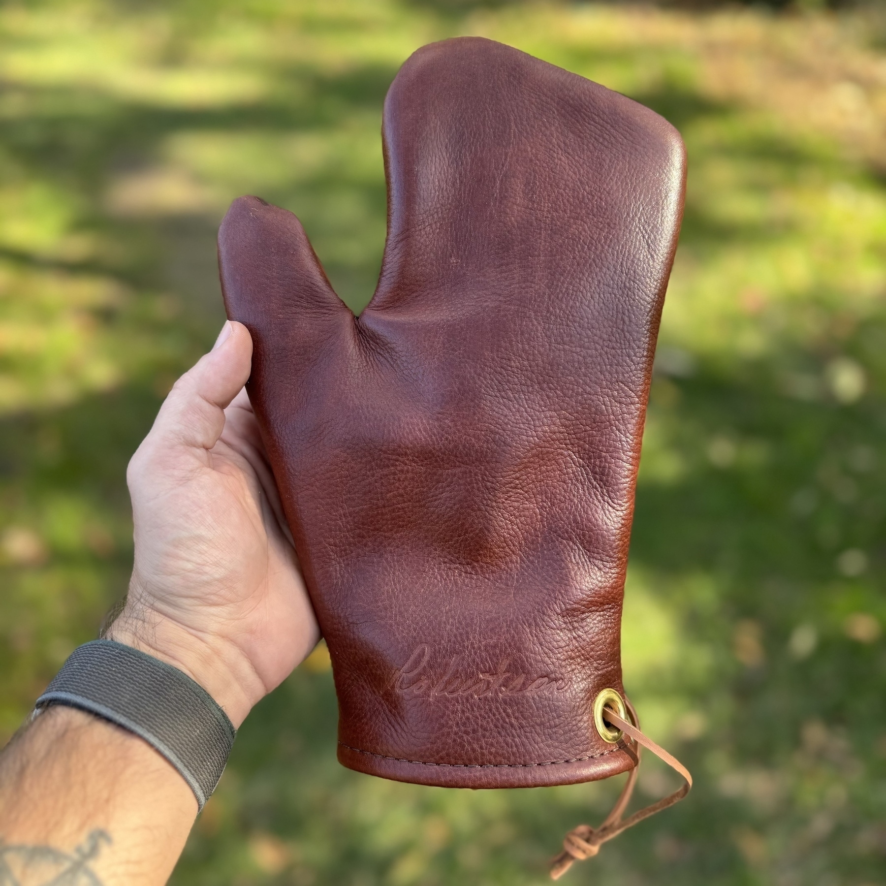 A person is holding a brown leather oven mitt outdoors.