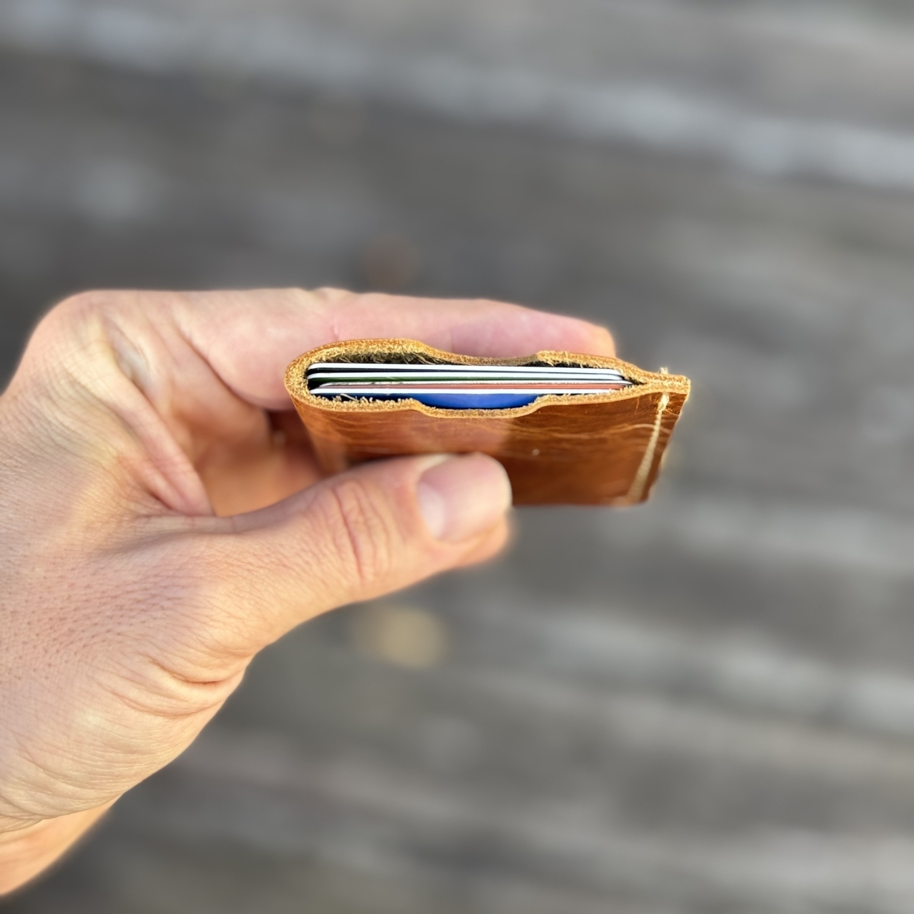 A hand is holding a slim, brown leather wallet containing a single card.