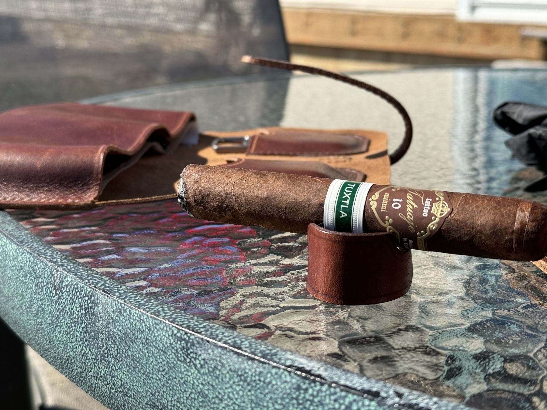 Tatuaje cigar on a handcrafted leather cigar stand in the foreground. Handcrafted leather cigar case seen in the background. 