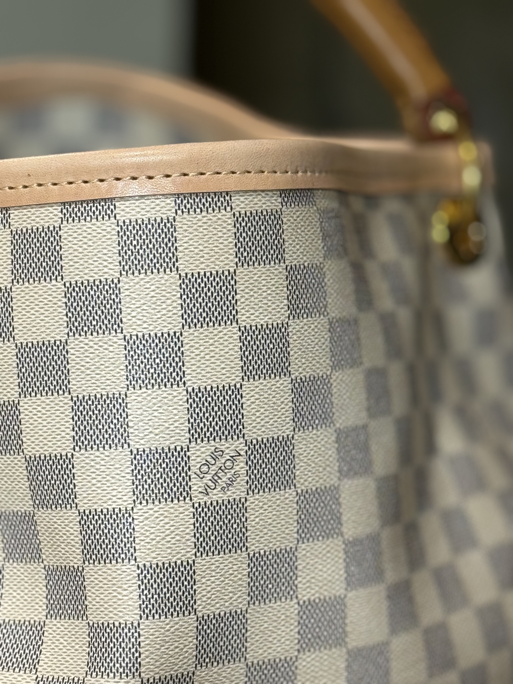 A close-up shot of a beige and white checkered and repaired handbag with a Louis Vuitton logo.