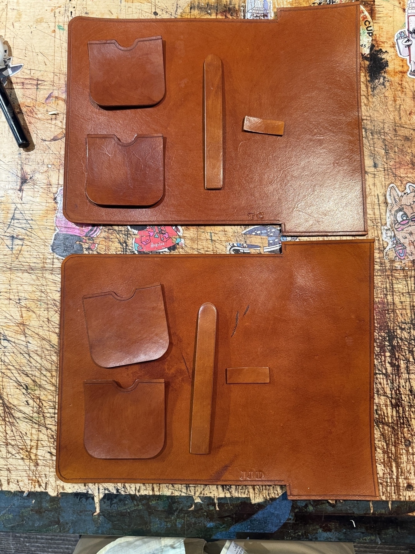 Two partially assembled leather cigar cases with pockets and straps placed on a wooden surface.