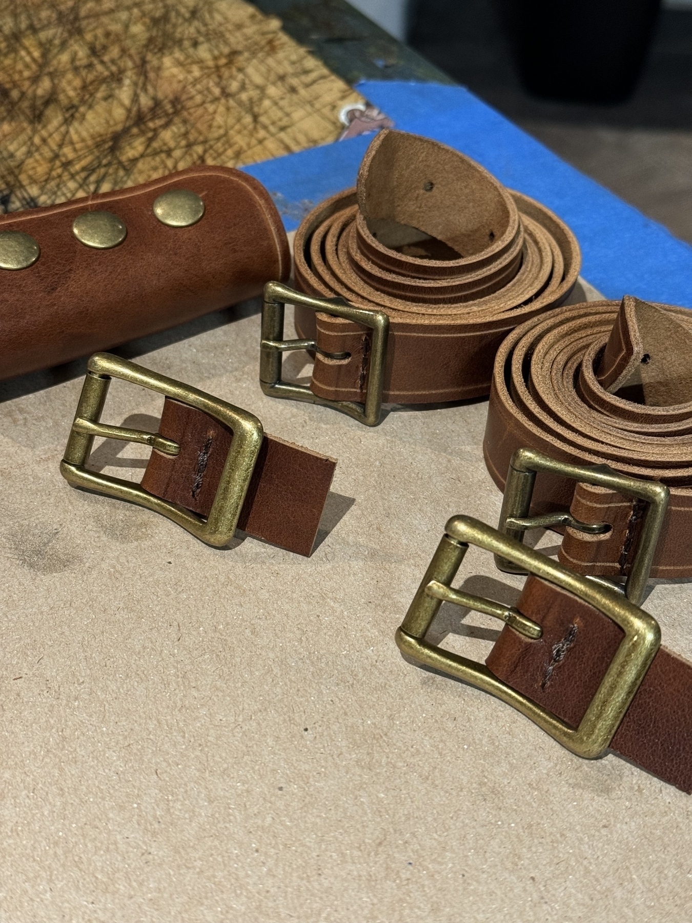 A set of leather belts with brass buckles, some rolled and others flat, are placed on a tabletop.