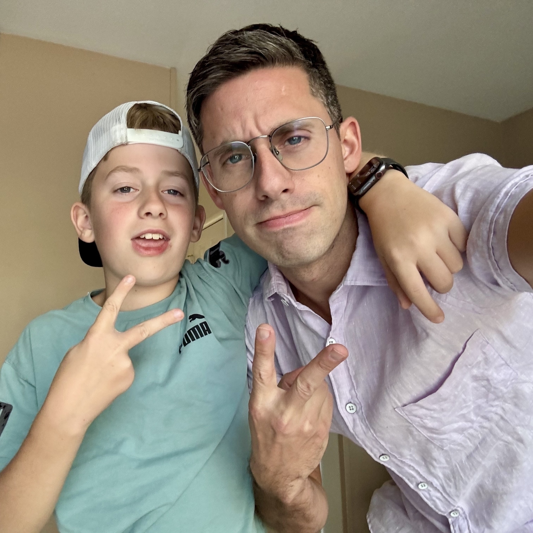 Two people making peace signs with their hands, one wearing a blue shirt and cap, and the other in a pink shirt and glasses.