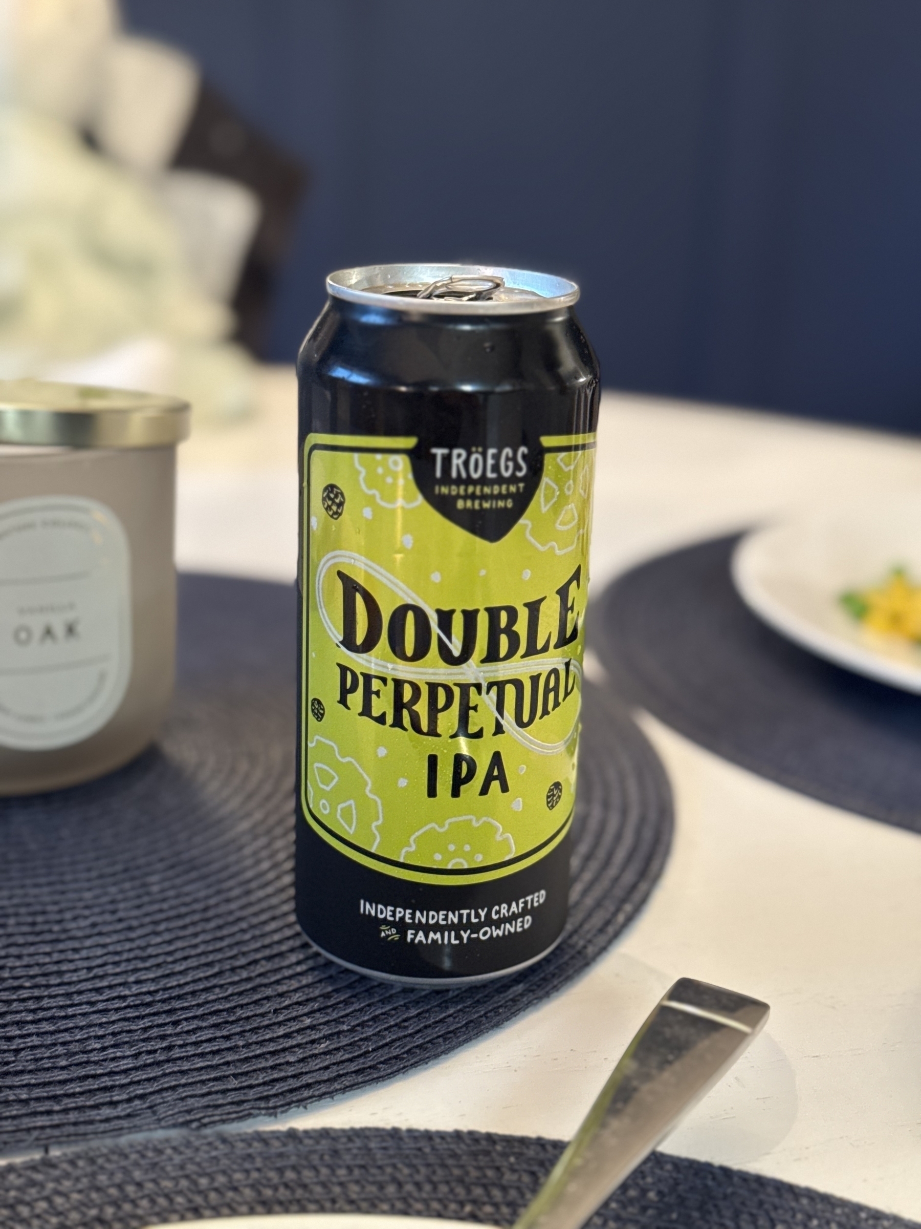 A can of Tröegs Double Perpetual IPA is placed on a table next to dishes and a candle.