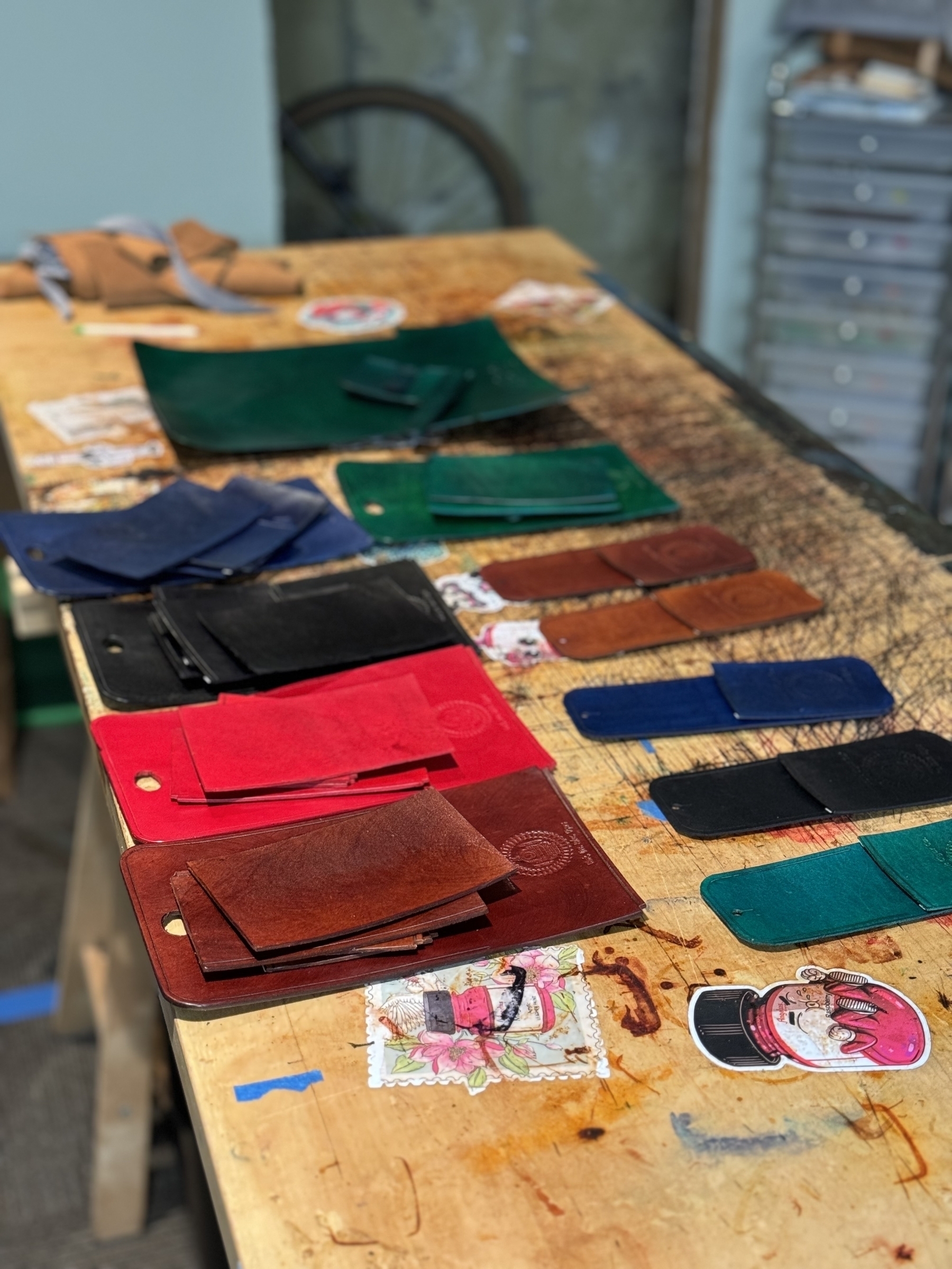 A workshop table is covered with various colorful leather pieces and some stickers.