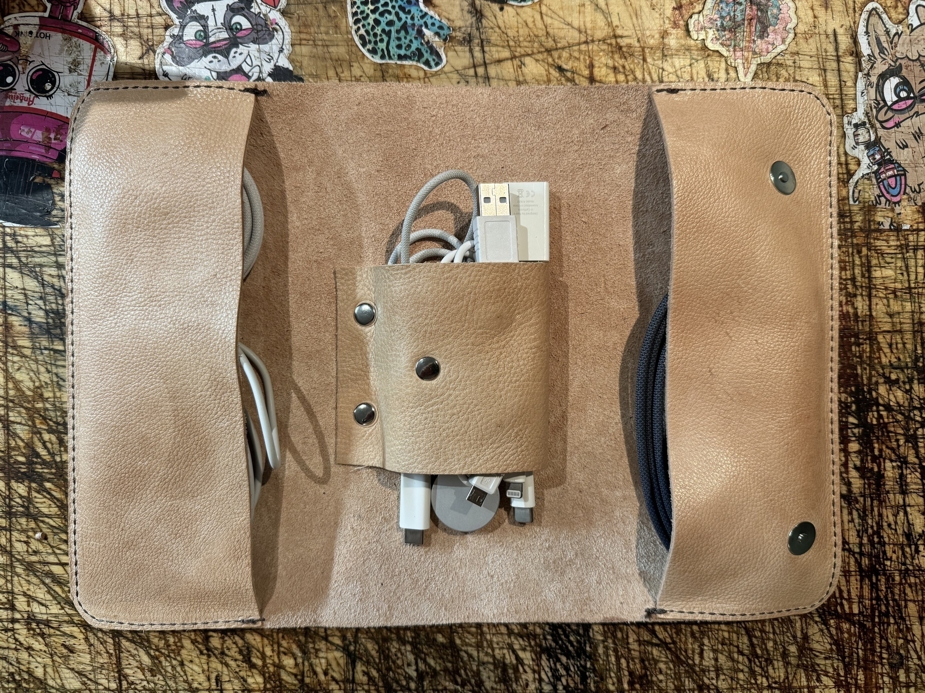 A beige leather case is open, displaying neatly organized cables and gadgets, with colorful patches in the background.