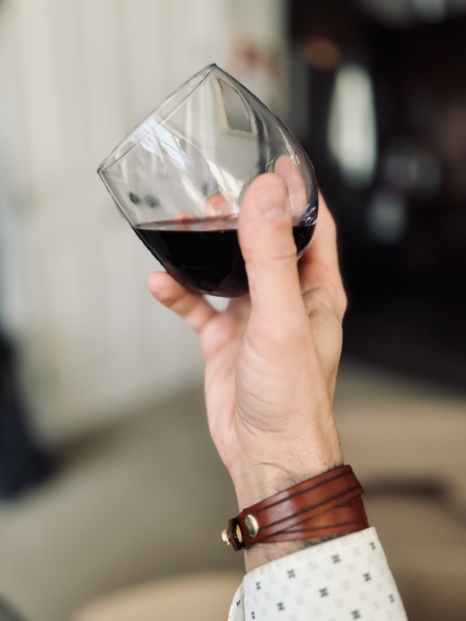 glass of red wine held in hand at an angle, an absolutely simple yet stunning men's leather bracelet visible on the wrist.