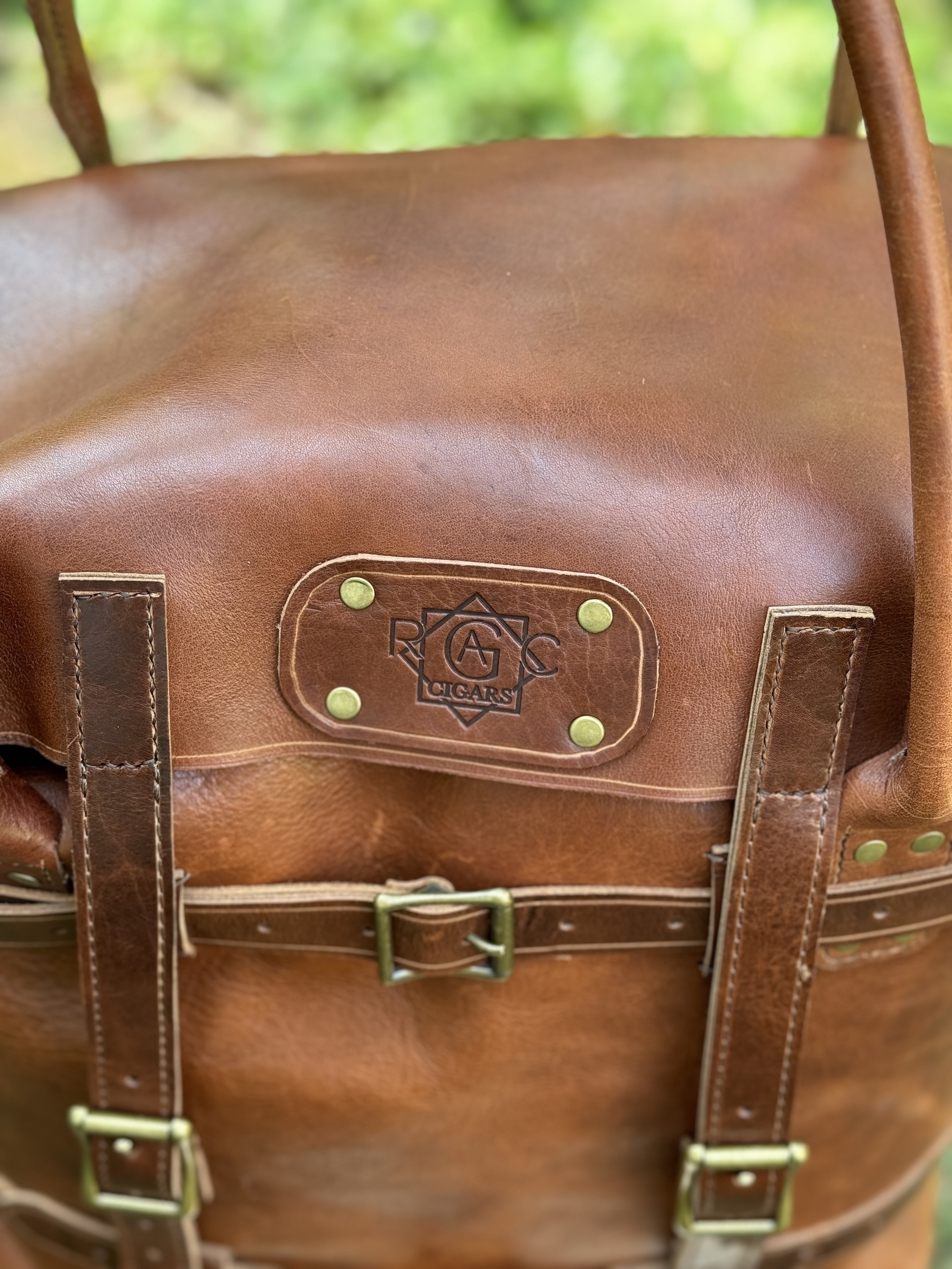 A close-up of a brown leather bag with a logo and straps visible.