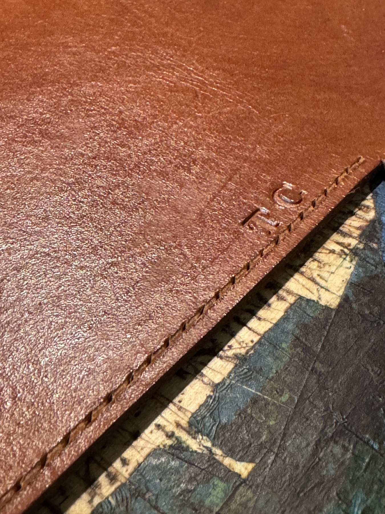 A close-up of a stitched, brown leather surface with the initials "T.C." embossed near the edge.