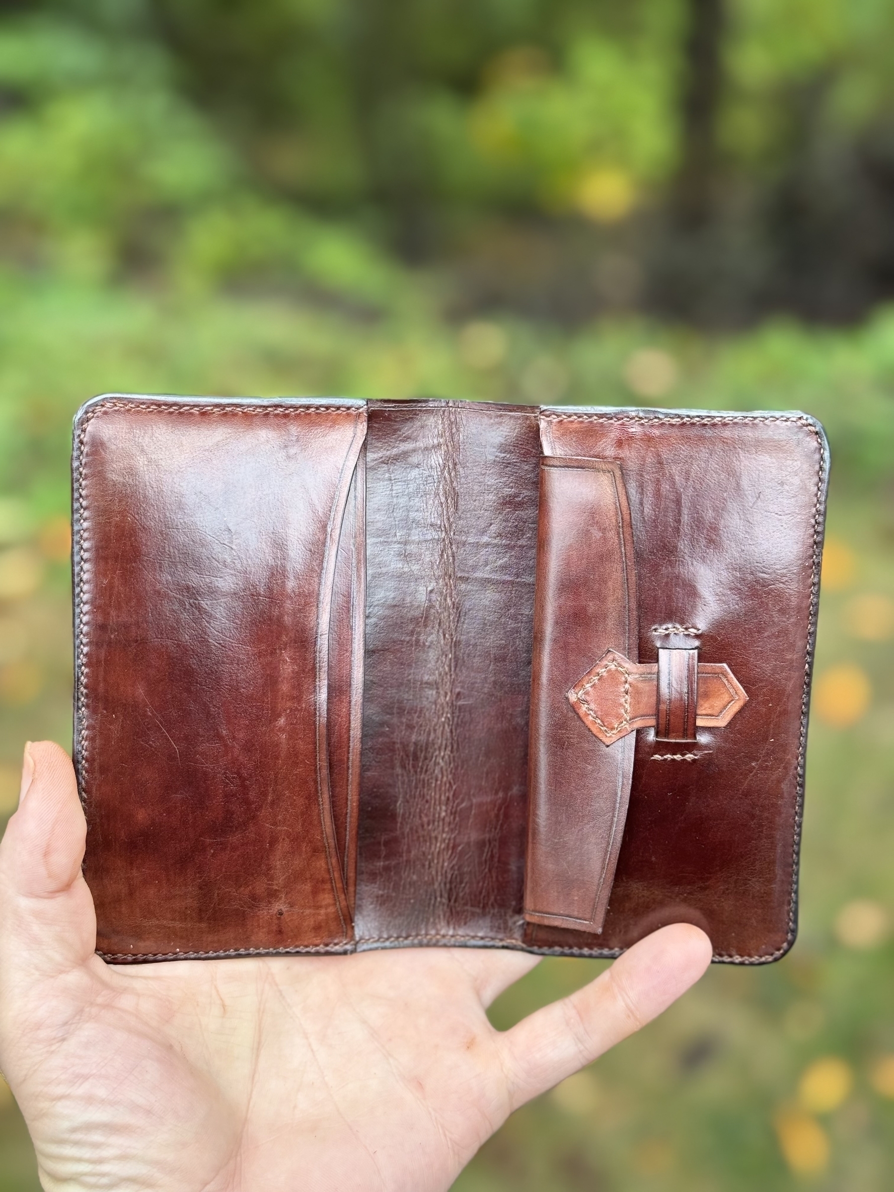 A hand is holding an open, empty brown leather wallet with visible stitching.