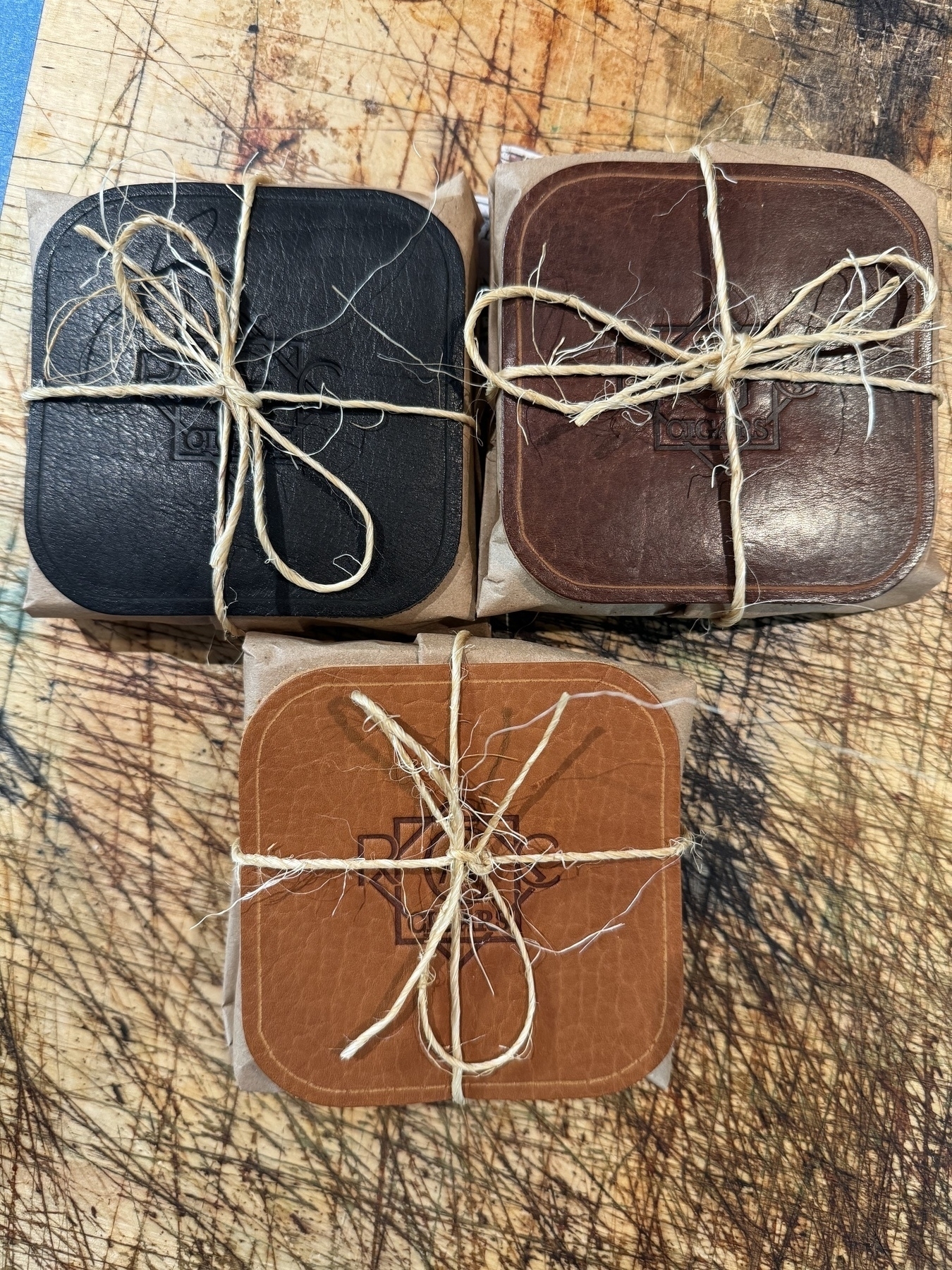 Three leather-wrapped packages tied with twine are arranged on a scratched wooden surface.