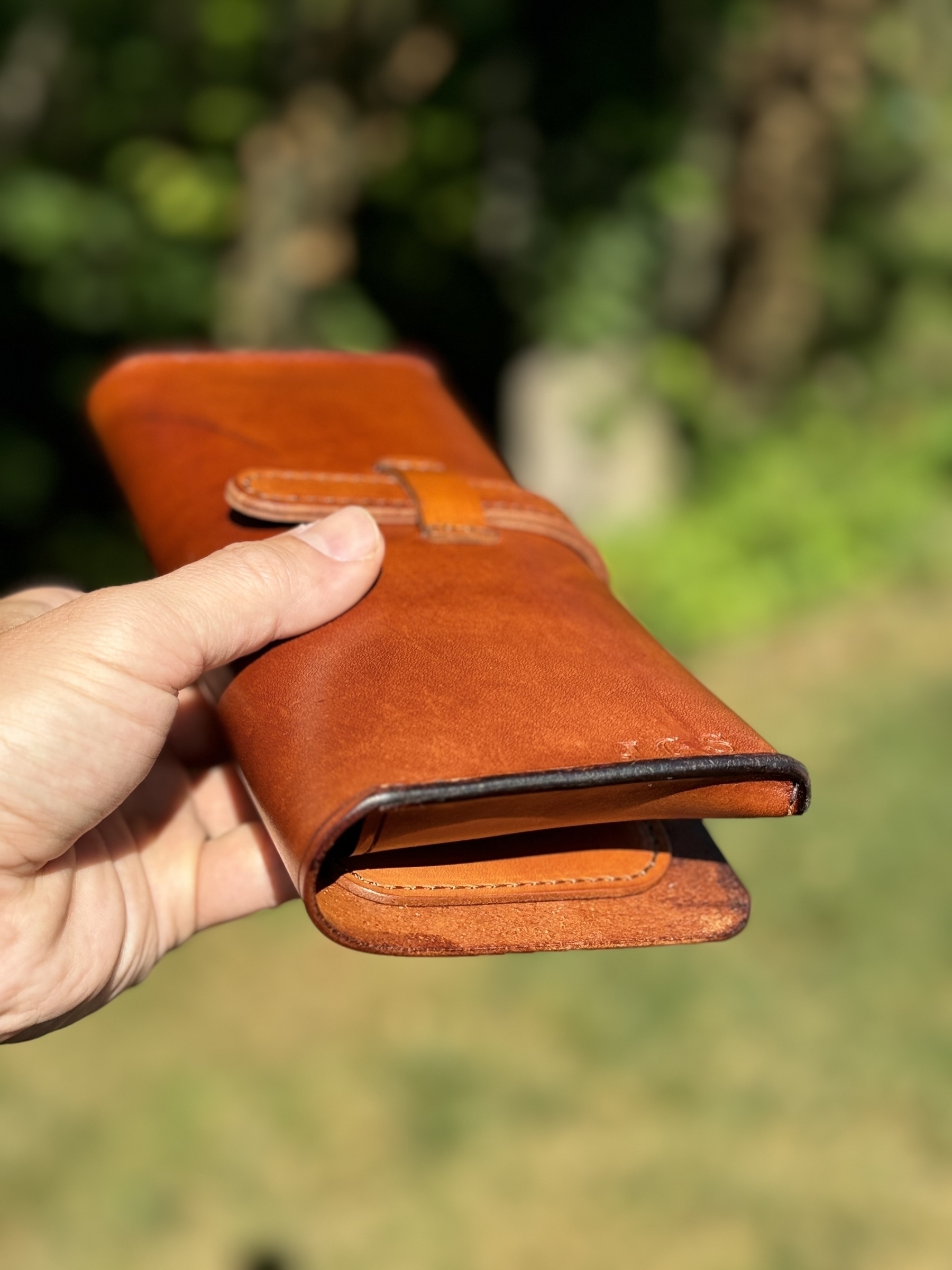 A person is holding a brown, leather cigar case outdoors.