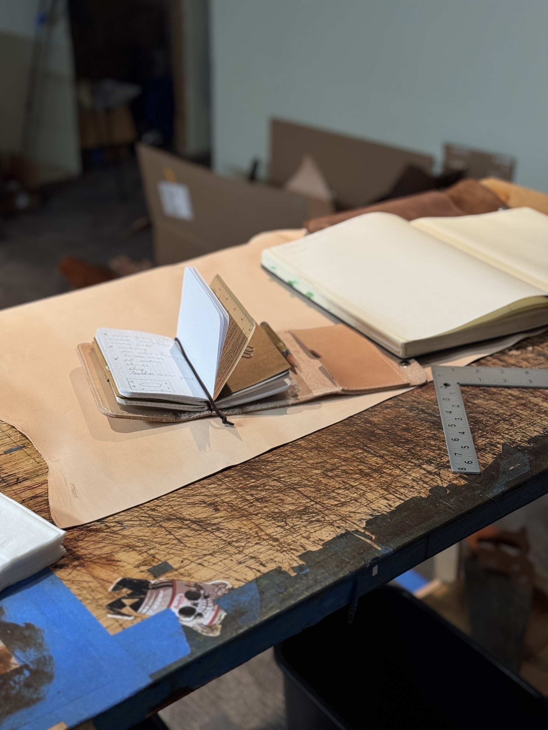 A workspace featuring an open sketchbook, a notebook, and a ruler on a wooden surface.