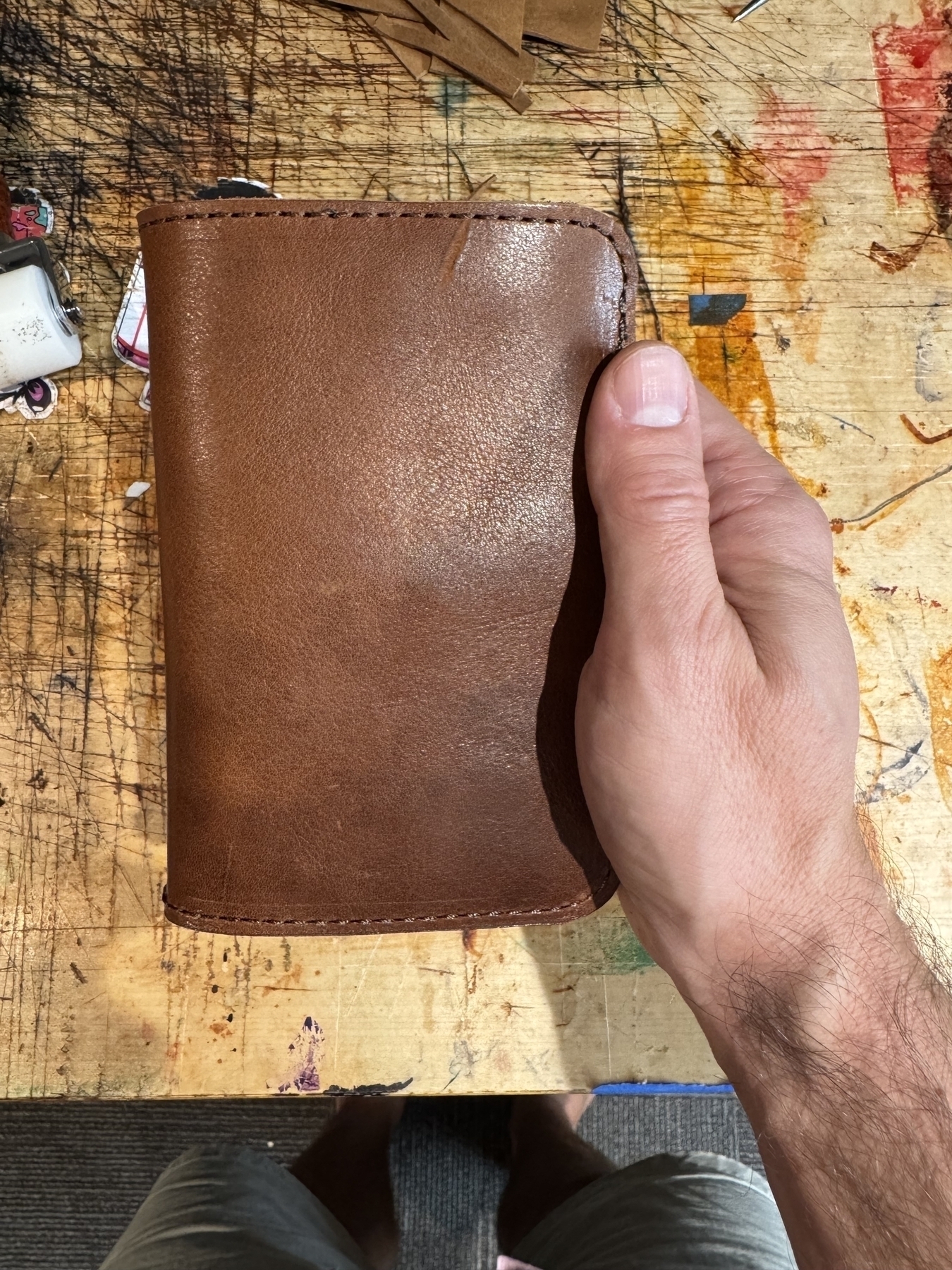 A hand is holding a brown leather wallet on a wooden table.