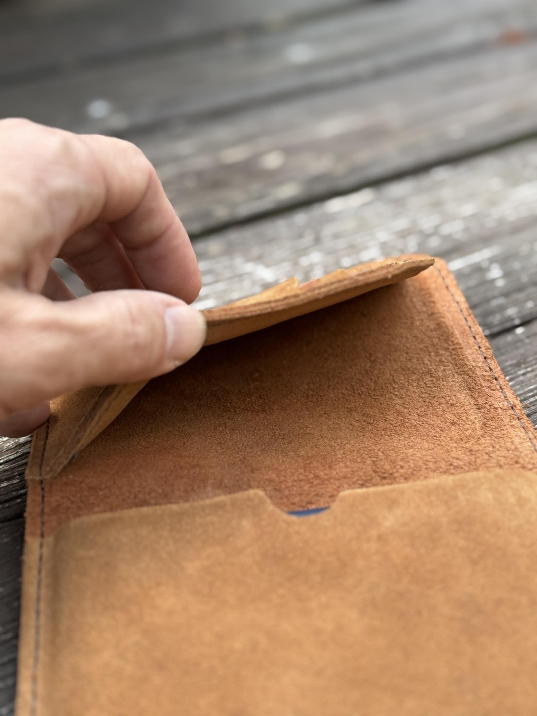 A hand is opening an empty brown leather passport case on a wooden surface.