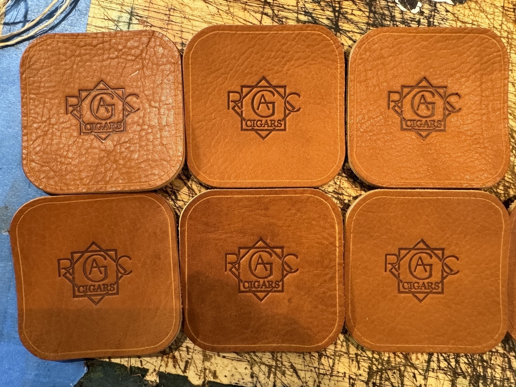 Six leather coasters are arranged in a grid pattern, each embossed with the logo "RAG Cigars."