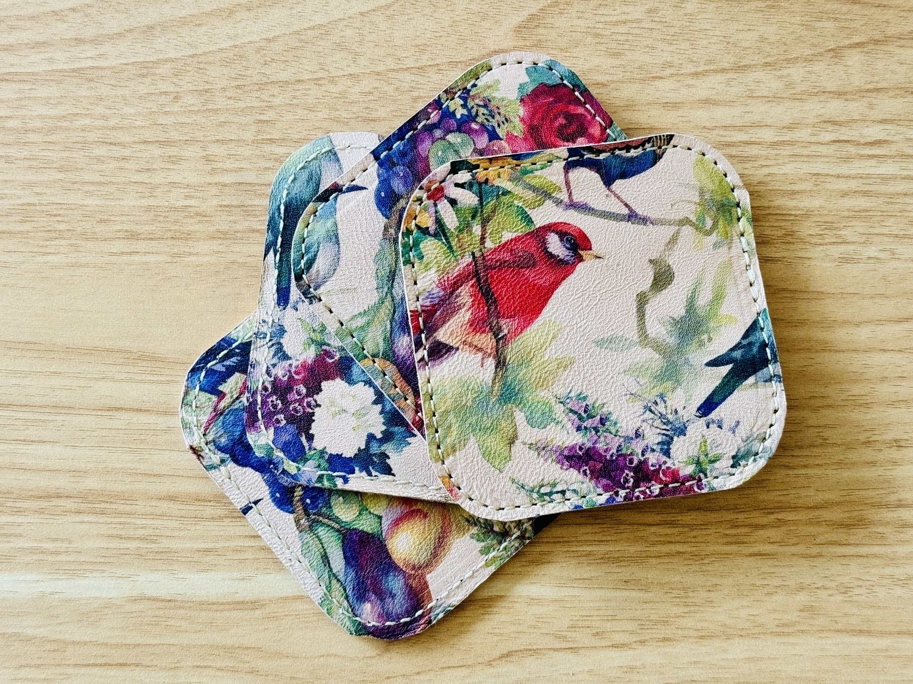 Four printed vet-tan sheepskin leather coasters, birds and flowers in a colorful symphony adorn.
