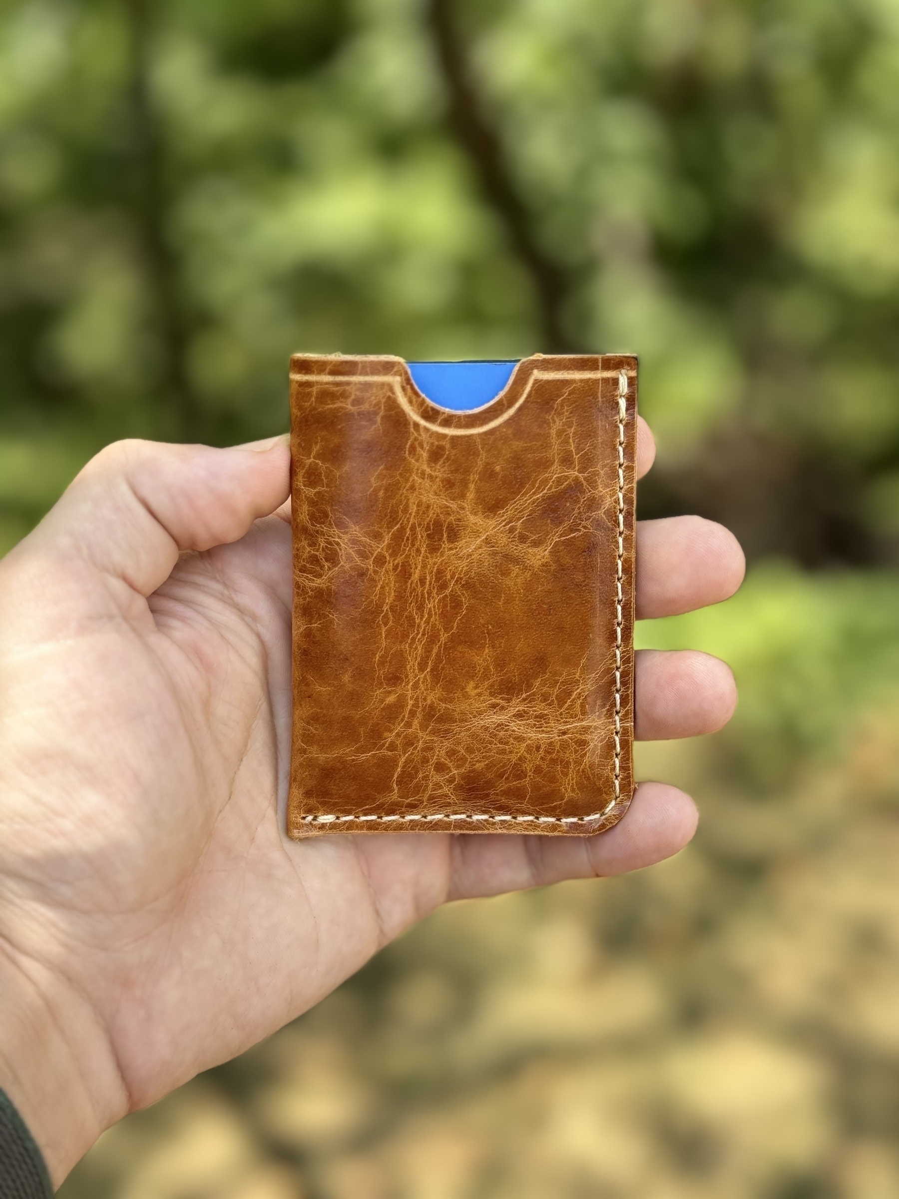 A hand is holding a brown leather card holder with a blue card partially visible inside.