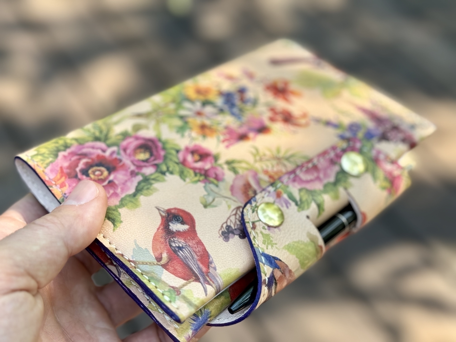 A hand is holding a floral-patterned wallet with button closures and a red bird design.
