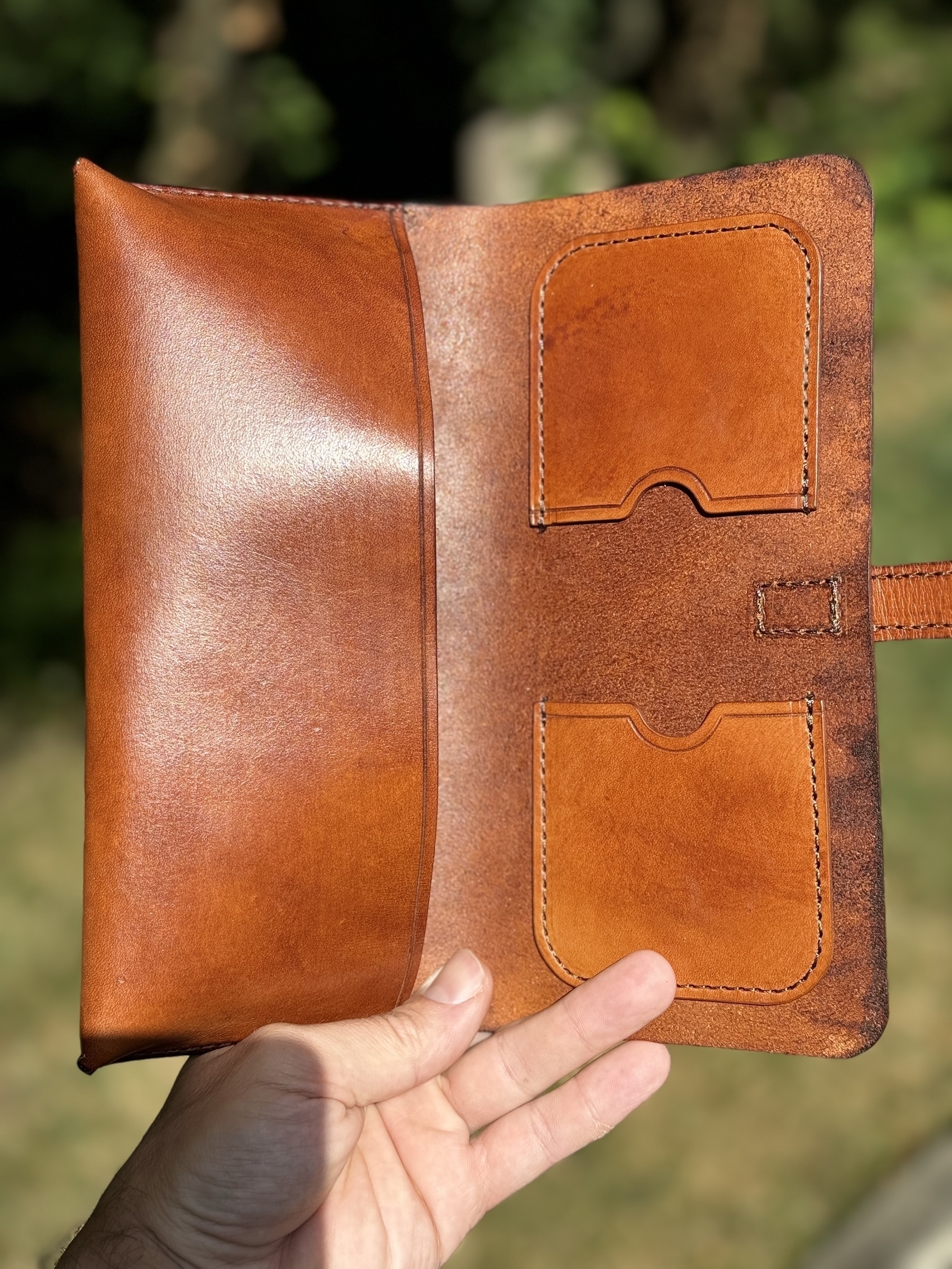 A hand is holding an open brown leather cigar case with cigar cutter and cigar cutter pockets and a large cigar pocket.