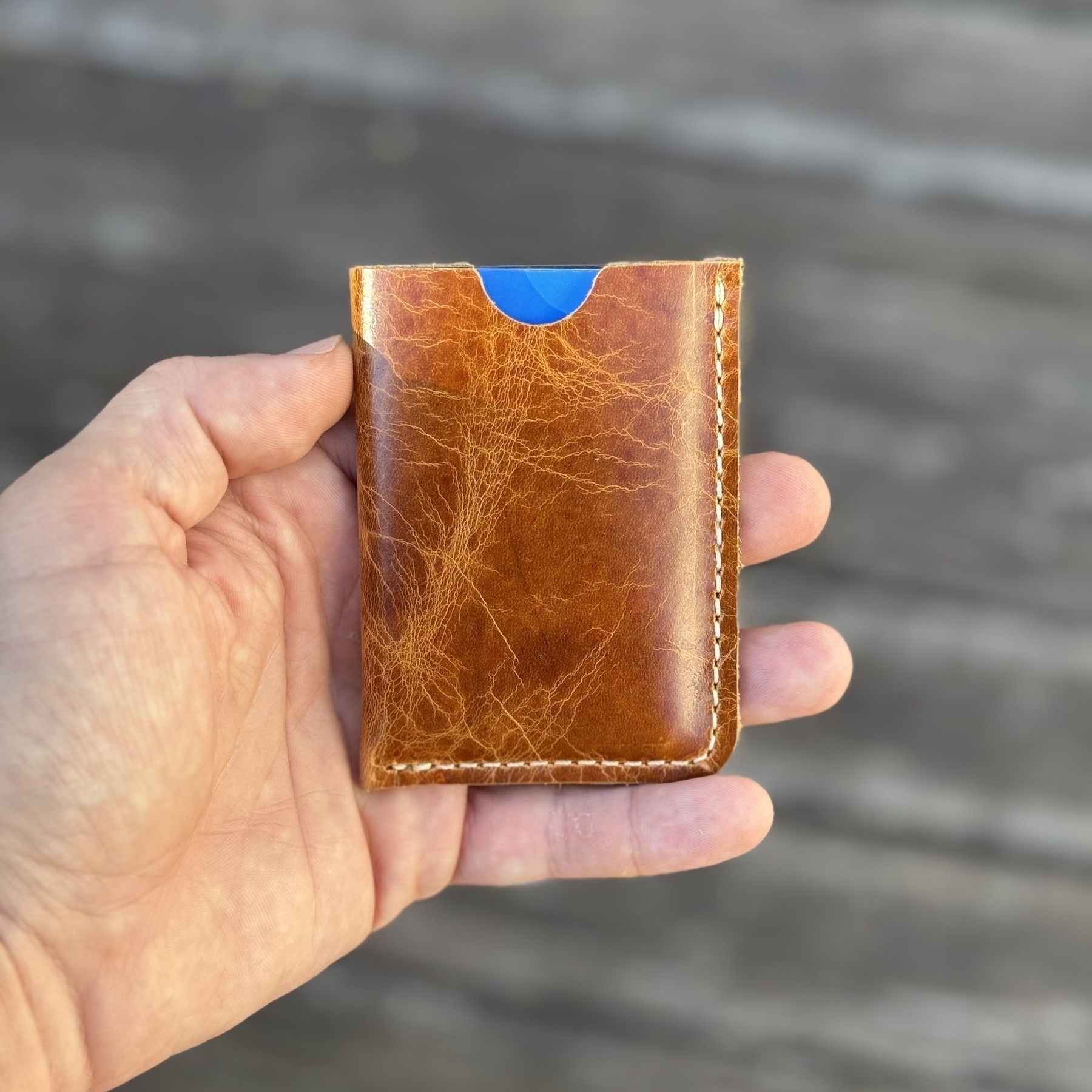 A hand is holding a brown leather wallet with a blue card peeking out.