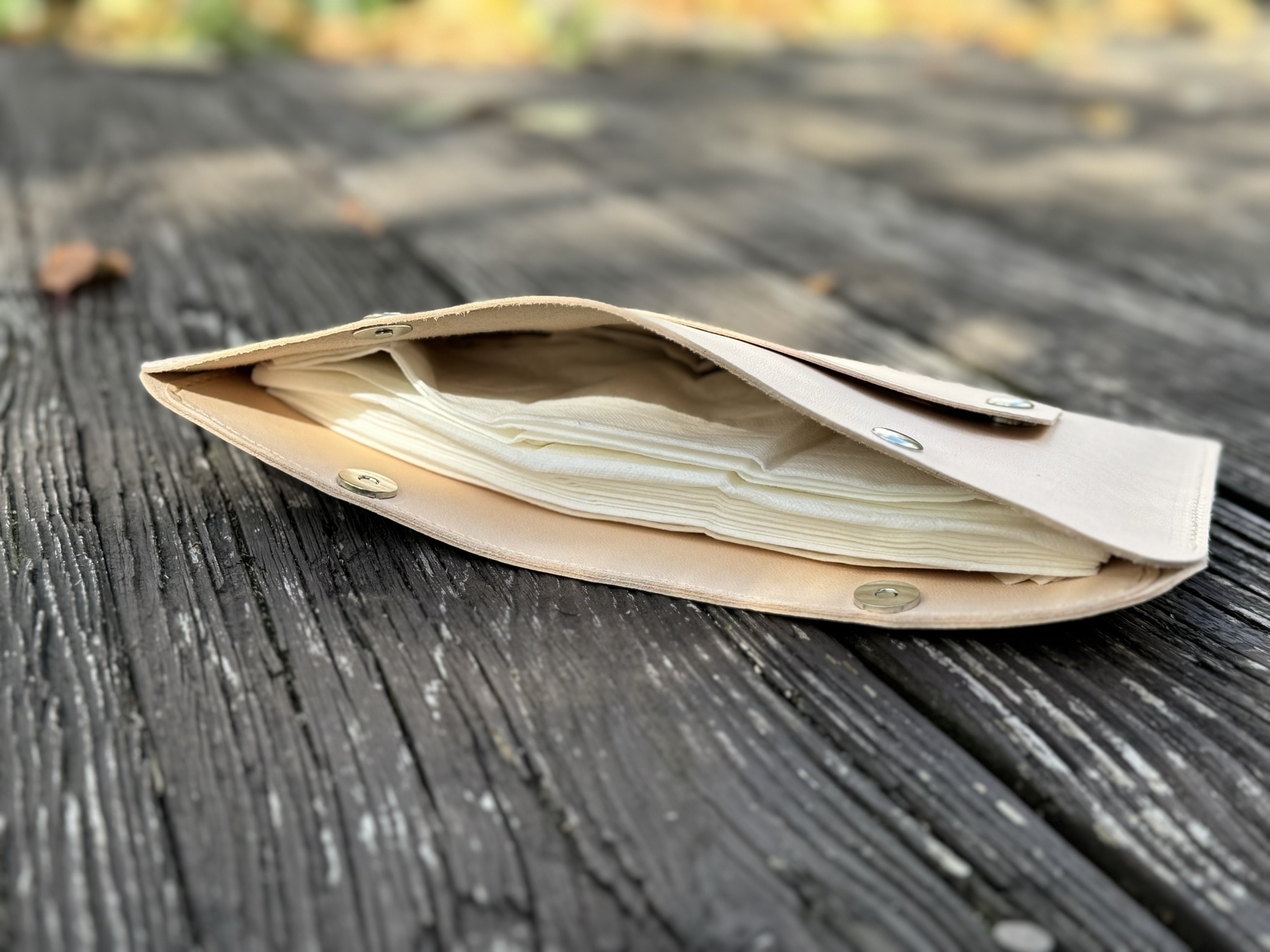 A beige clutch purse lies open on a wooden surface, revealing its contents.