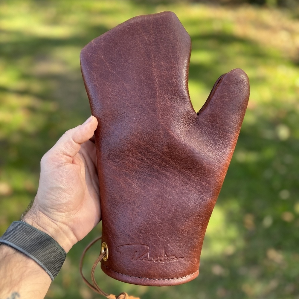 A person is holding a brown leather mitt in an outdoor setting.