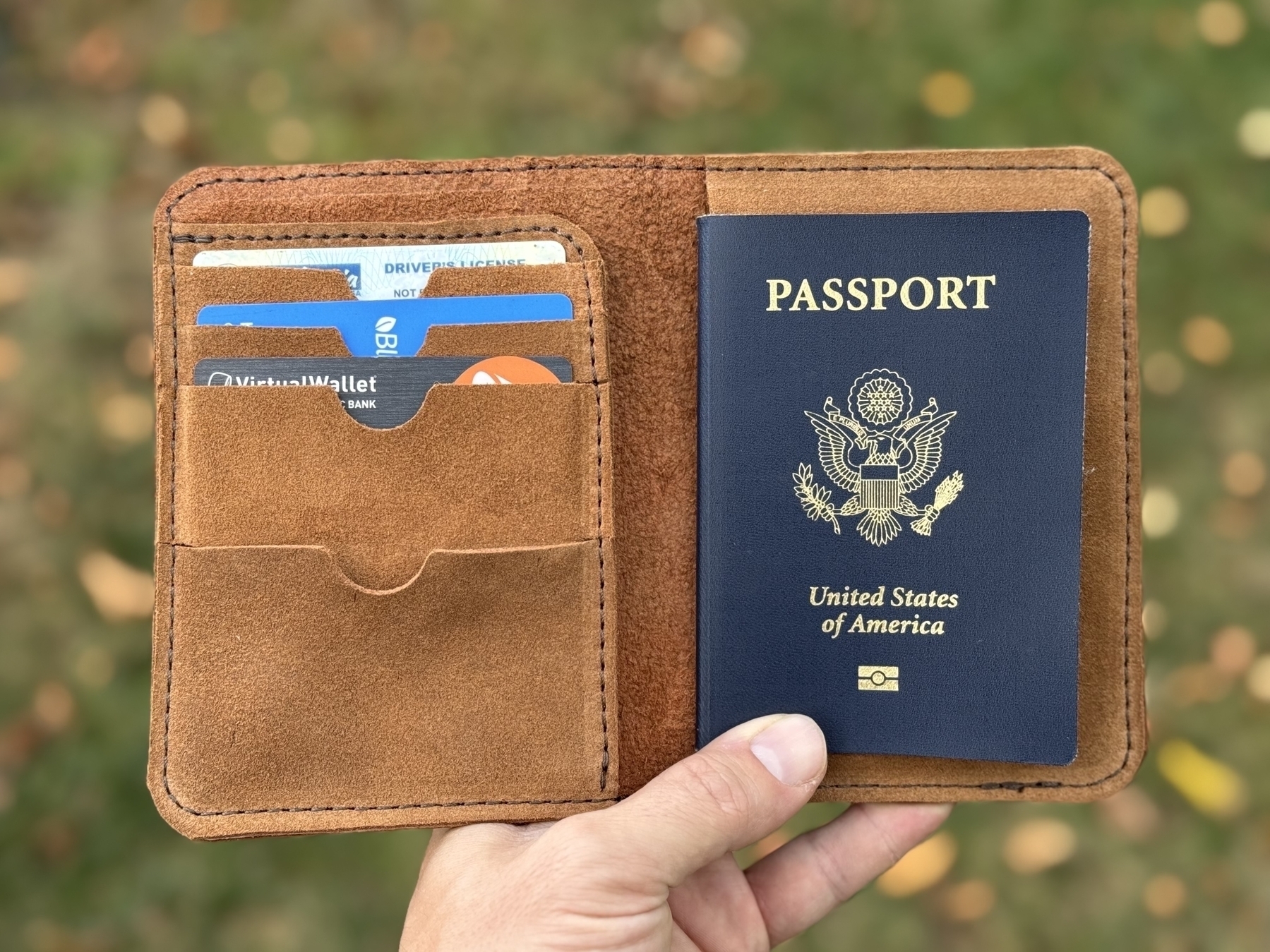 A hand is holding an open leather passport case containing a U.S. passport and multiple credit cards.