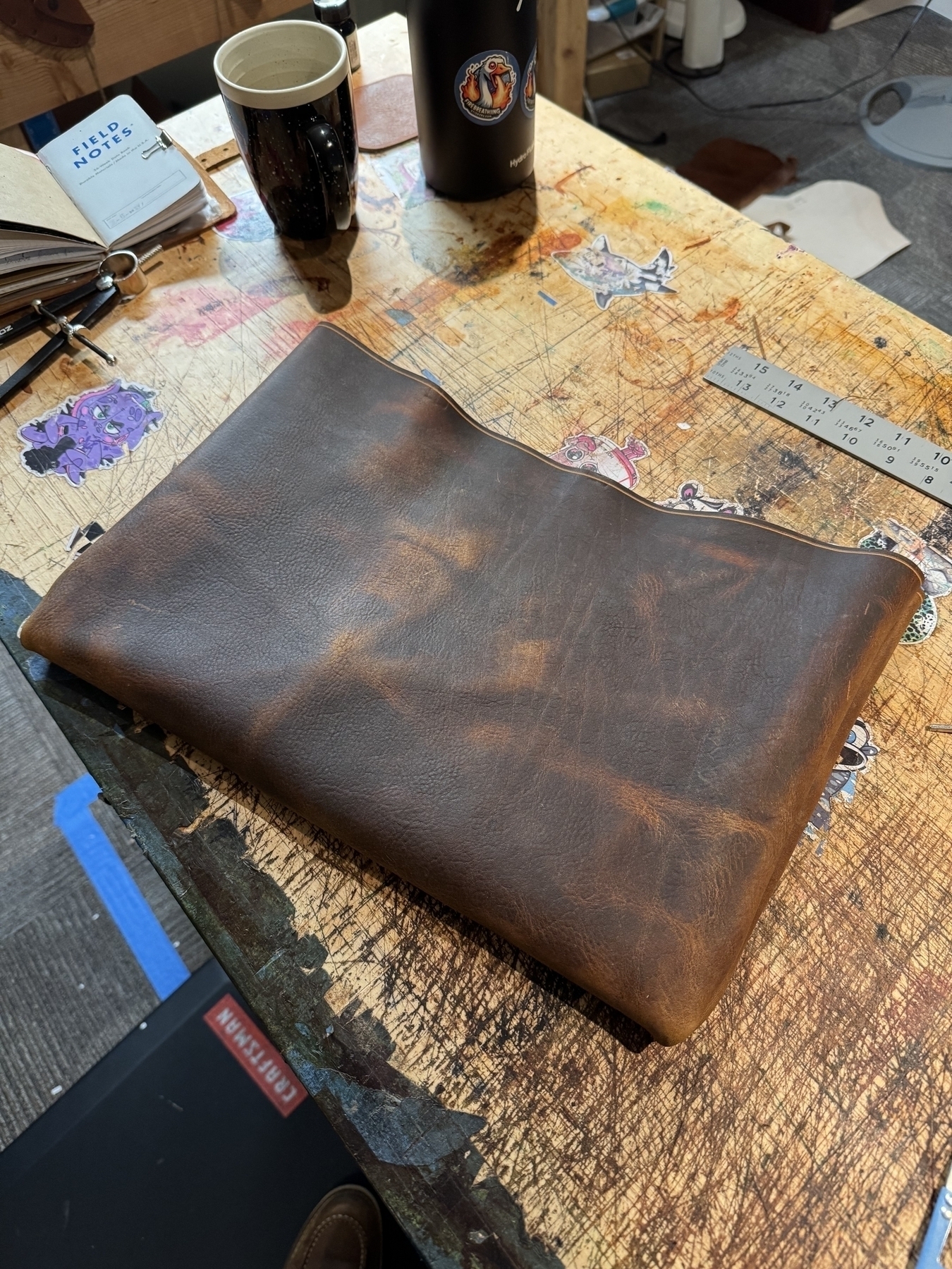 A brown leather sleeve is resting on a cluttered workbench alongside various tools and items.