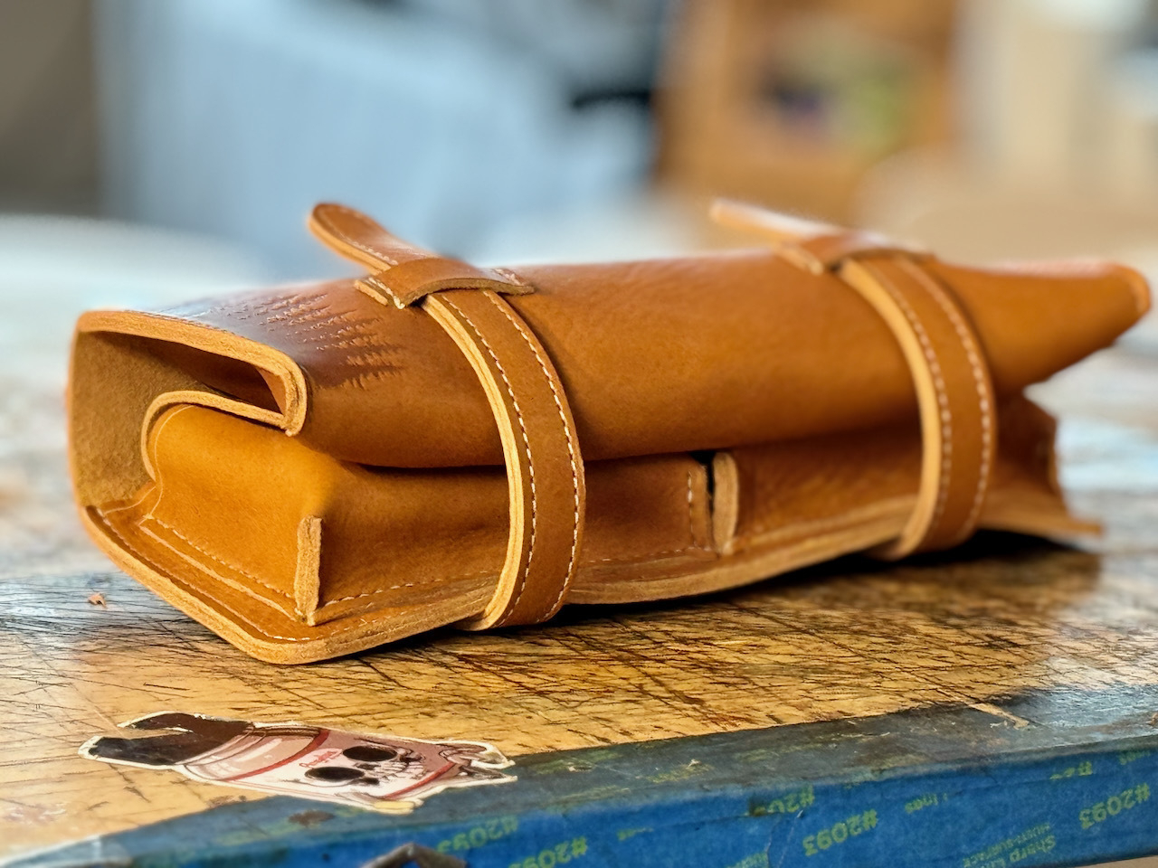 The leather boveda cigar case shown closed. Two long straps from the back tuck under loops on the front of the case to keep it securely closed. pine tree engraving is visible on the bottom of the front.