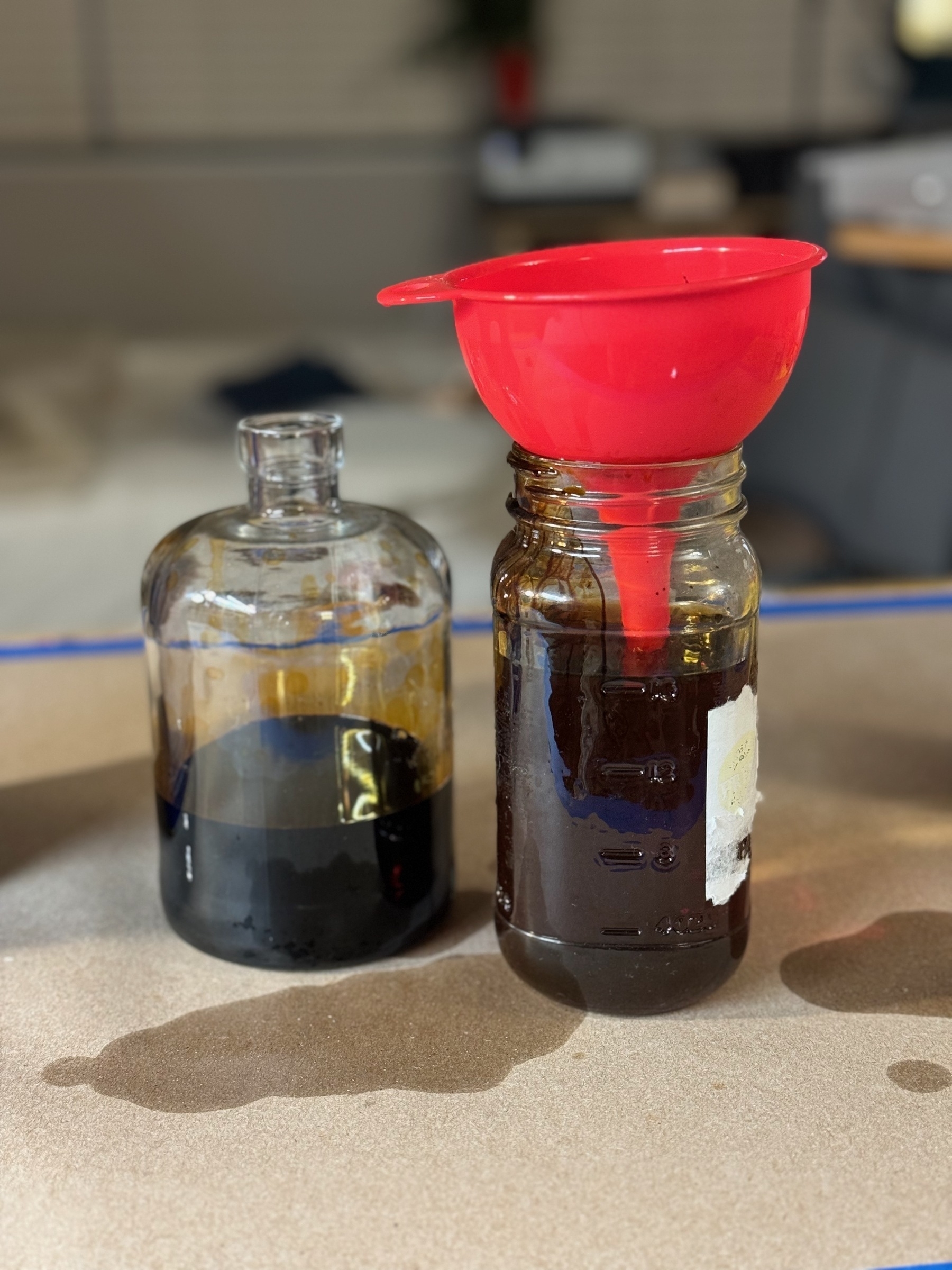 two glass bottles on a table, one with a funnel protruding from the top.