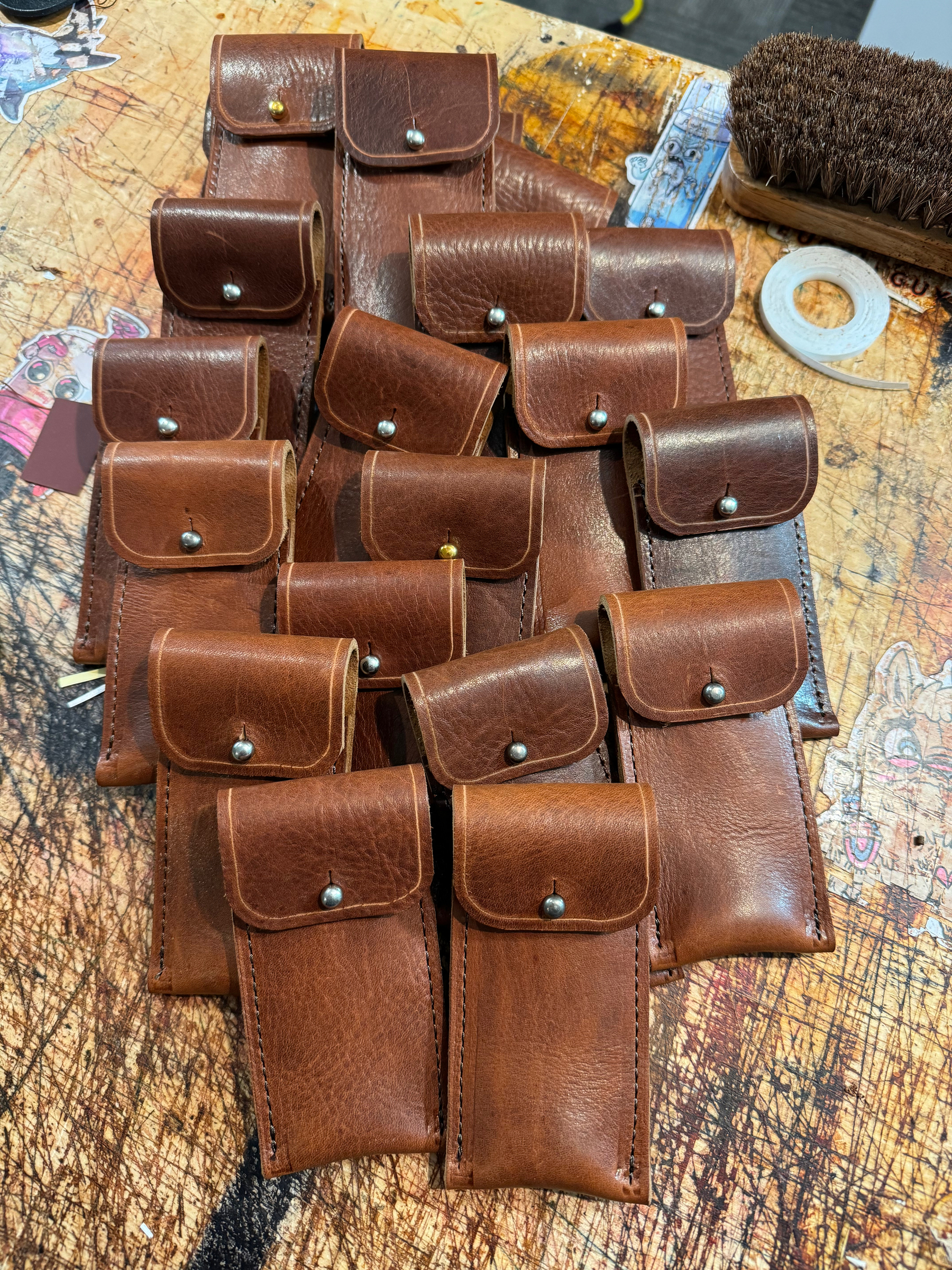 A collection of brown leather pouches with snap buttons is neatly arranged on a distressed wooden surface.