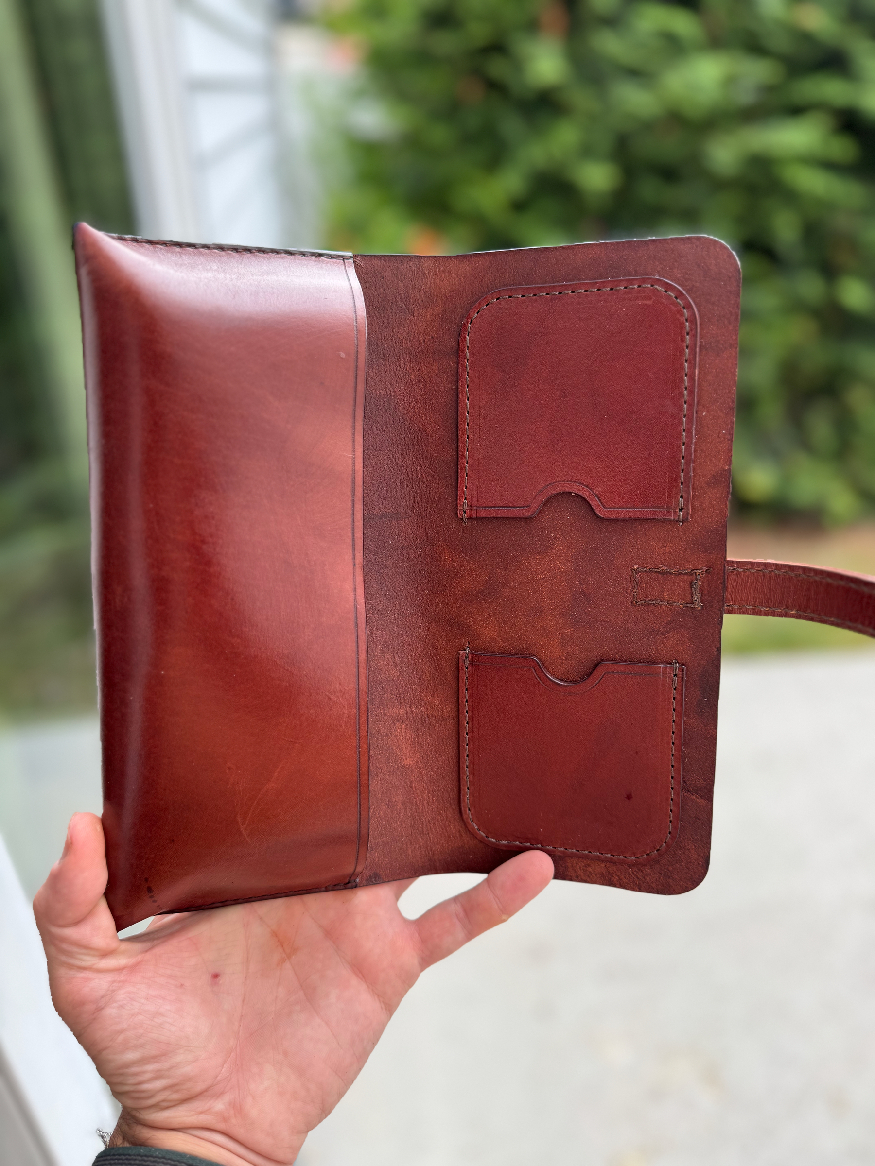 A hand is holding an open leather wallet with card slots and a cash compartment, set against a blurred outdoor background.