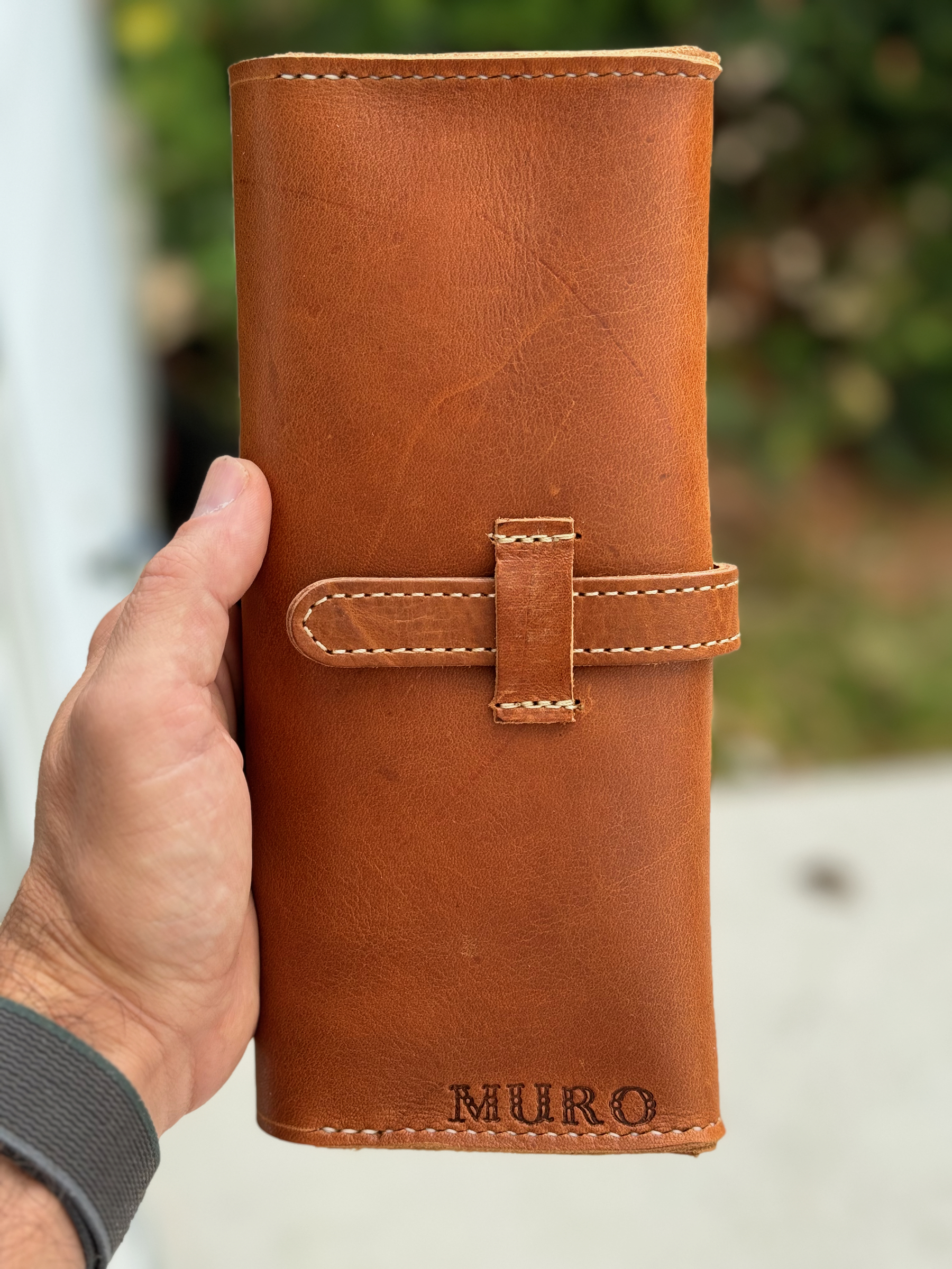 A person is holding a brown leather wallet or case embossed with the word "MURO."