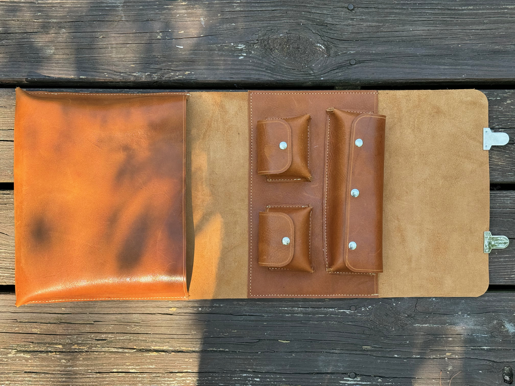 An open leather cigar case with multiple compartments and a buckle, displayed on a wooden surface.