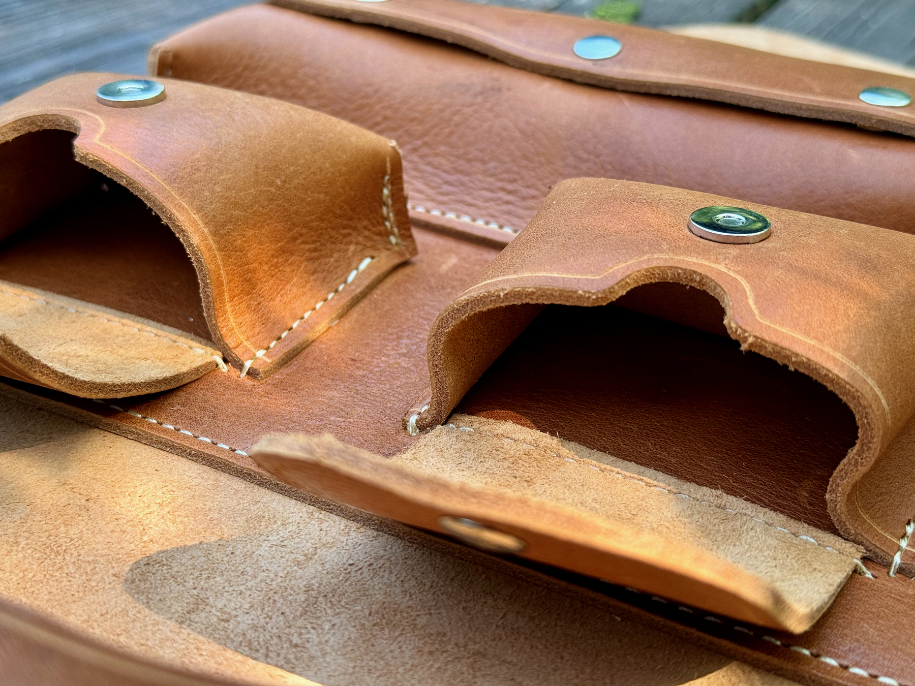 A close-up view of an open leather cigar case reveals compartments for cigar lighter and cigar cutter with snap closures and visible stitching.