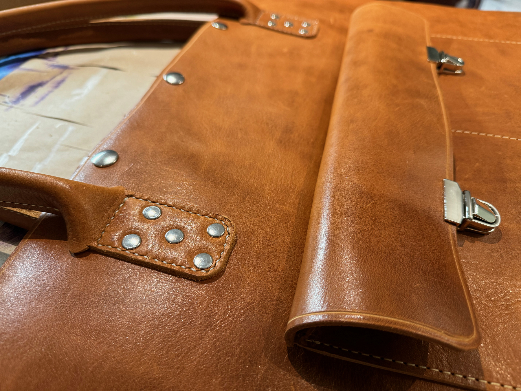 A close-up view of a brown leather bag showcases its smooth texture, metallic rivets, and buckles.