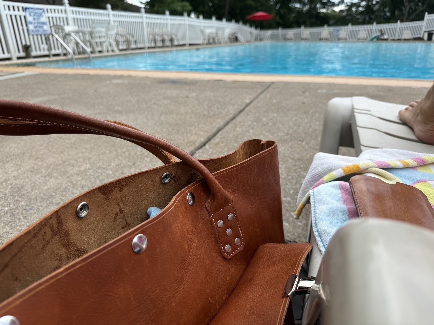 Person sitting by a pool with a brown leather bag next to them.
