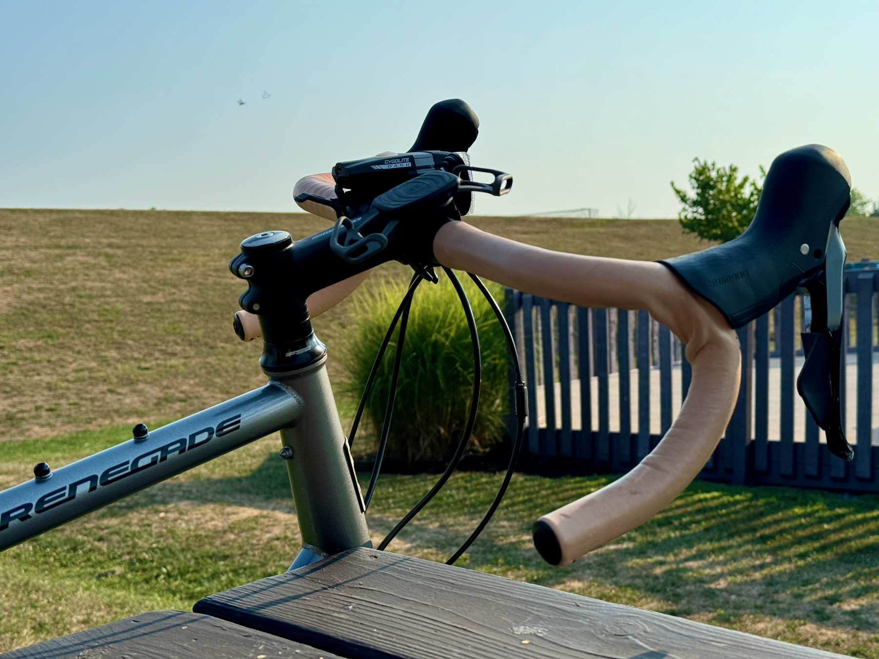 A bicycle with leather wrapped handlebars is parked near a wooden fence in a grassy area.